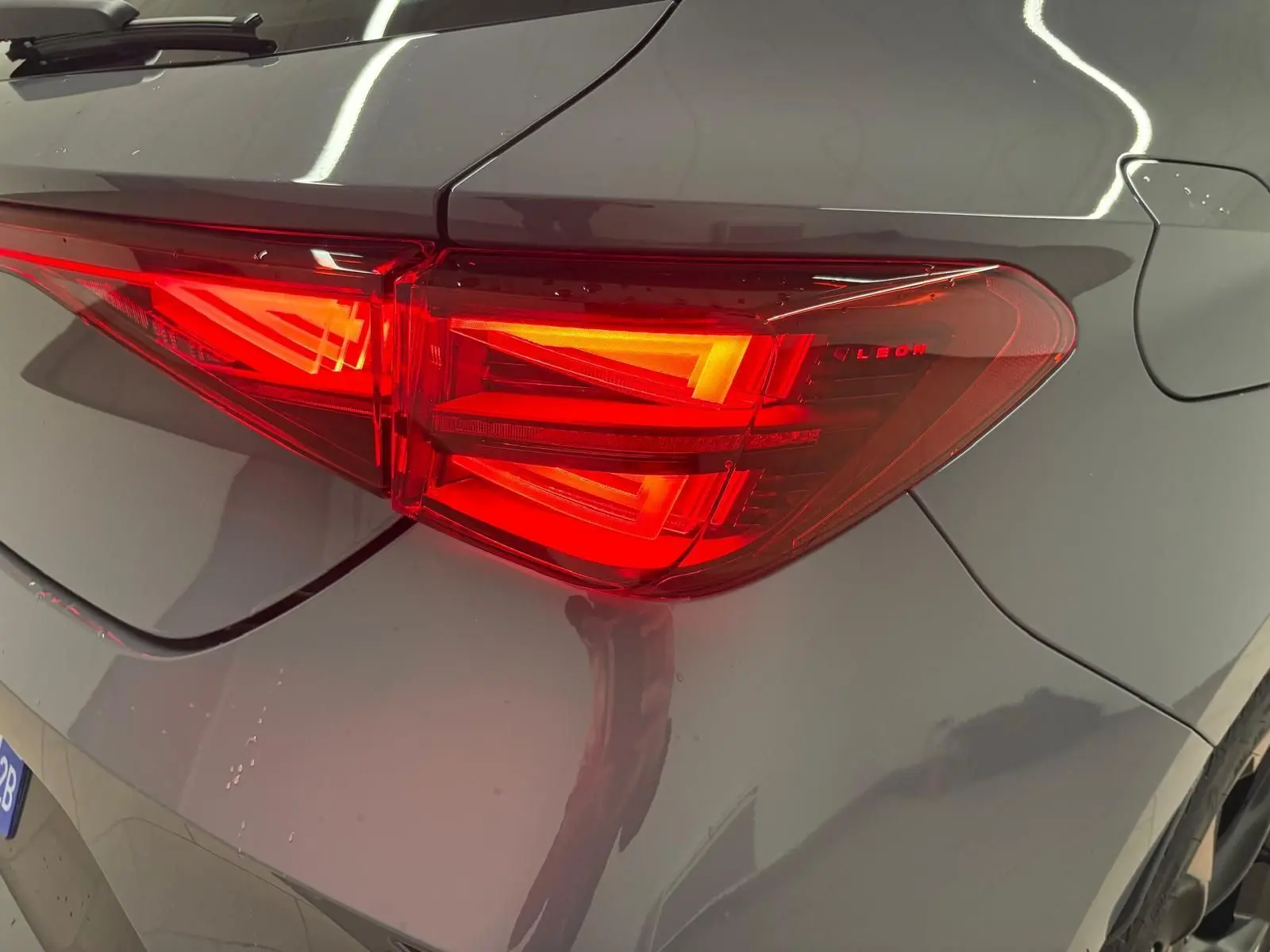 Gros plan sur le feu arrière droit rouge vif d'une CUPRA Leon 2025 gris Graphène avec jante cuivrée visible.