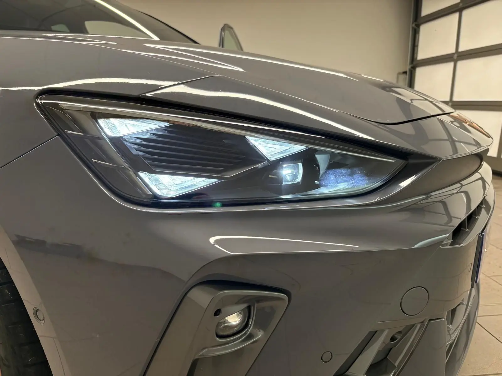 Gros plan sur le phare avant droit gris Graphène du CUPRA Leon 2025 avec éclairage LED et partie du pare-chocs visible.