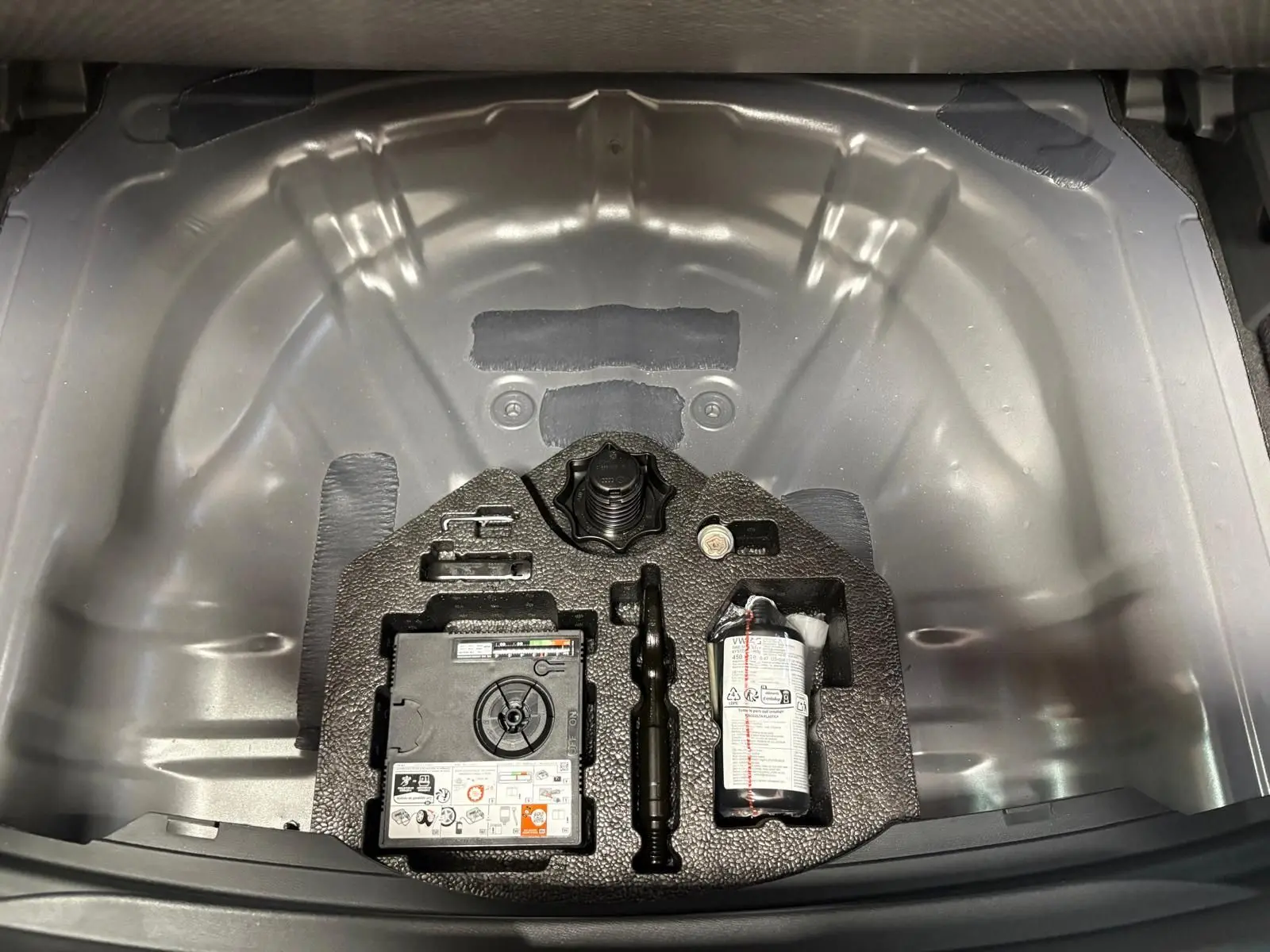 Vue plongeante sur le coffre ouvert d'une CUPRA Leon 2025, montrant le rangement métallique gris et les outils intégrés.