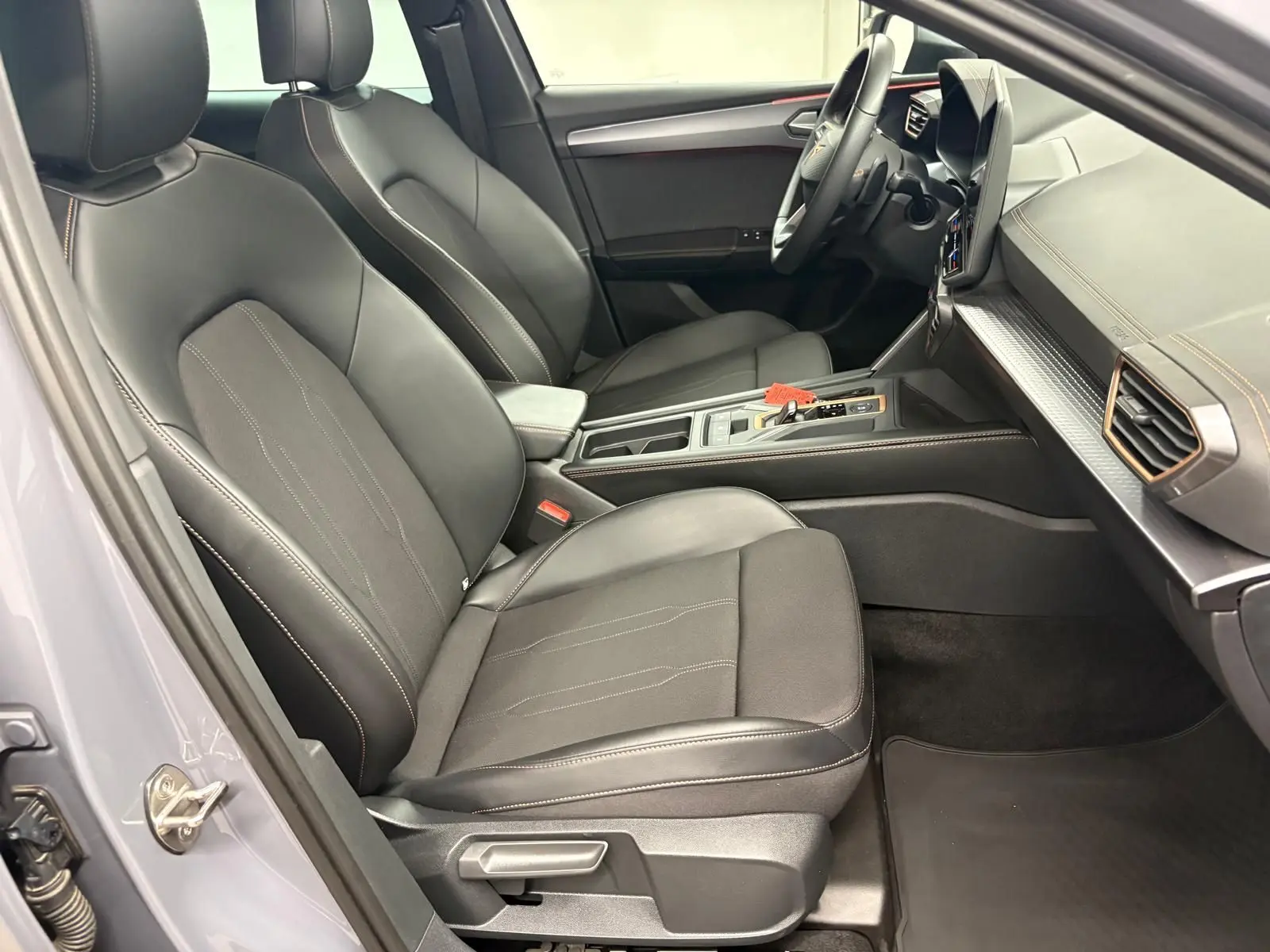 Vue intérieure côté conducteur de la CUPRA Leon 2025 avec sièges noirs, coutures contrastées et tableau de bord moderne.