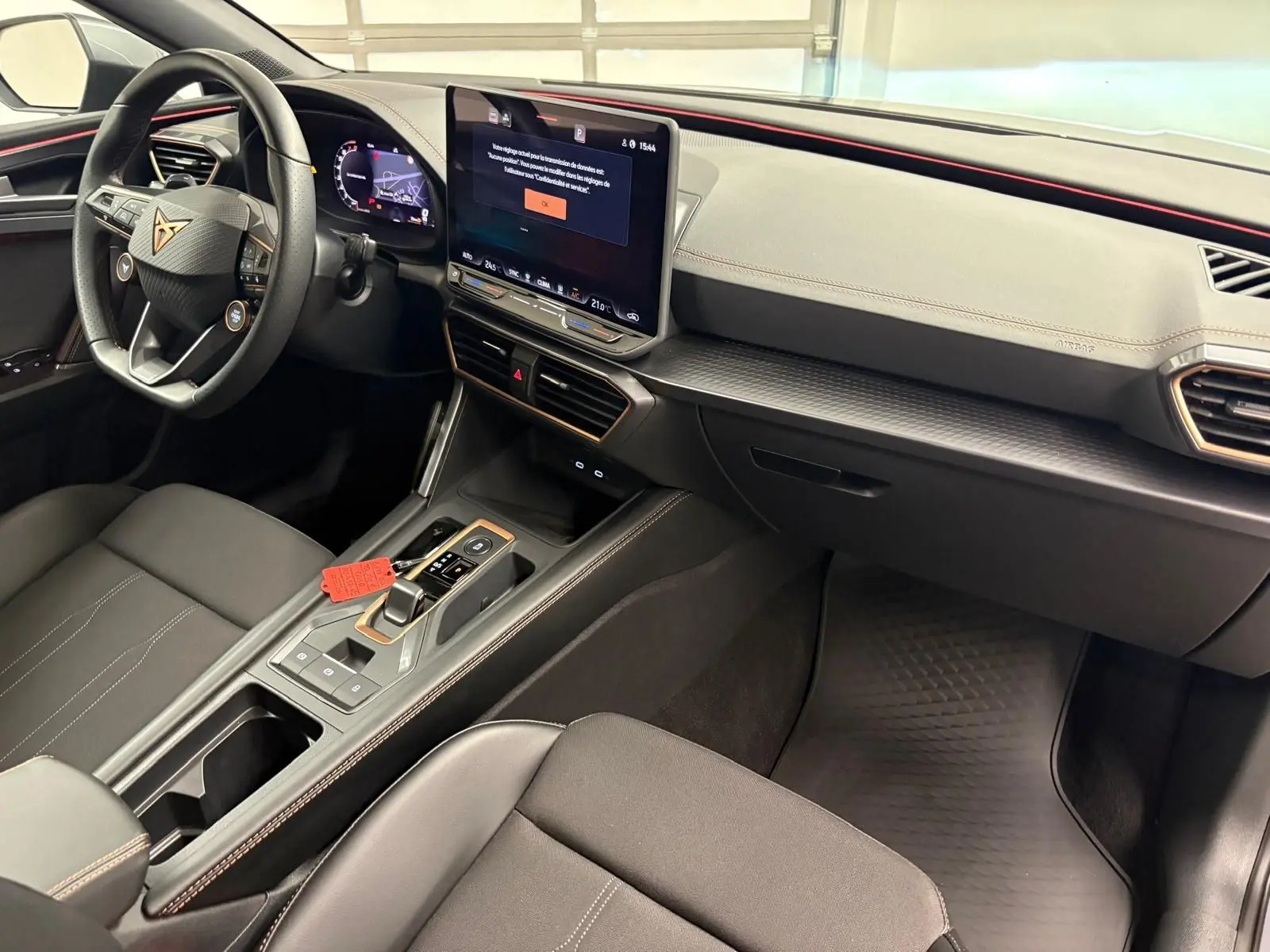 Intérieur de la CUPRA Leon 2025 vu côté passager, tableau de bord noir avec écran central tactile et volant sport.