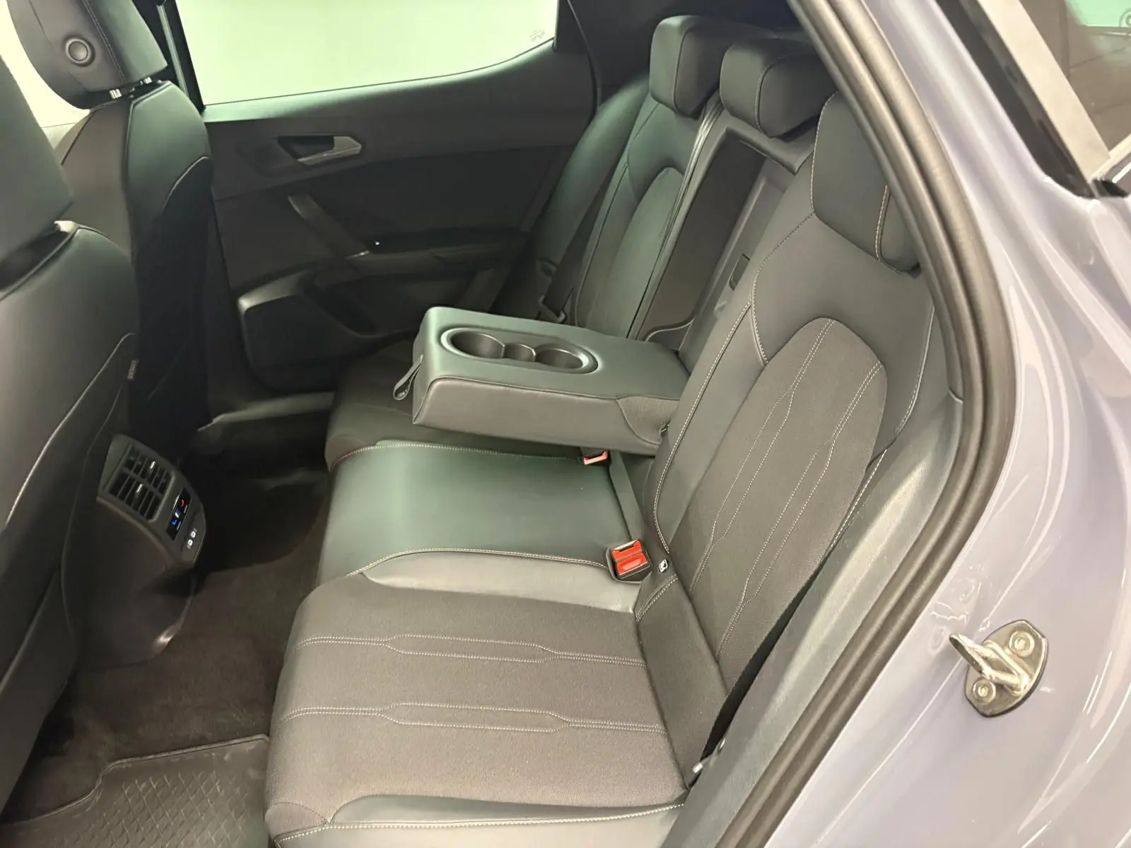 Vue côté droit de l'intérieur arrière gris foncé de la CUPRA Leon 2025 avec accoudoir central et porte ouverte.