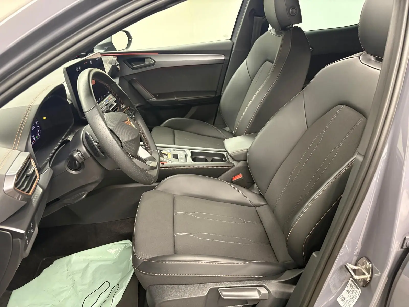 Vue intérieure côté conducteur de la CUPRA Leon 2025 gris Graphène, sièges cuir noirs avec surpiqûres contrastées.