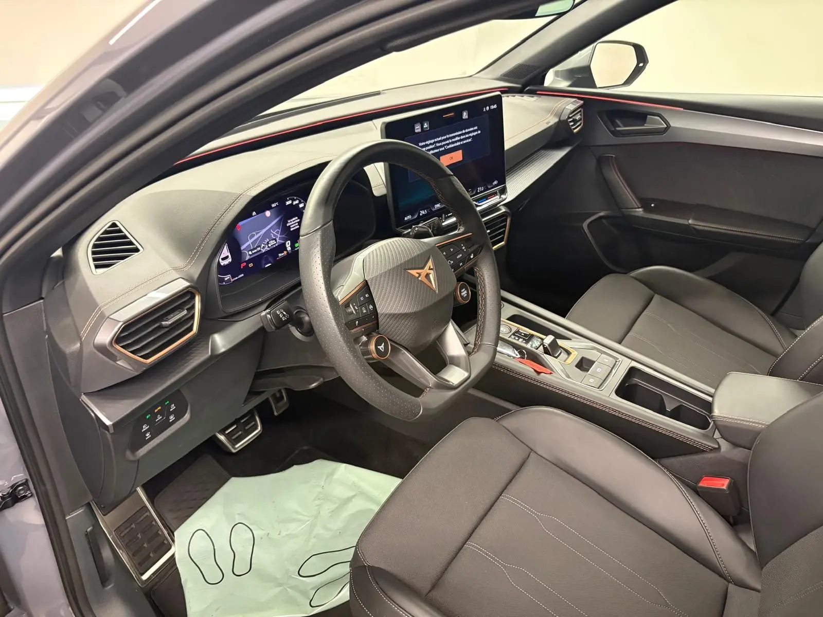 Vue intérieure côté conducteur de la CUPRA Leon 2025 gris Graphène, avec volant multifonction et écran central tactile.