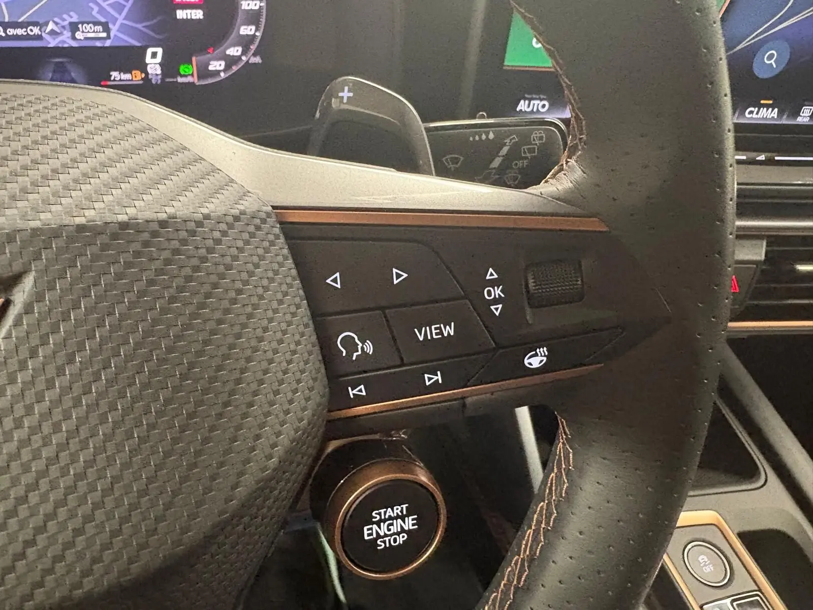 Gros plan sur le volant cuir noir avec surpiqûres cuivrées et commandes multifonctions du CUPRA Leon 2025, tableau de bord en arrière-plan.