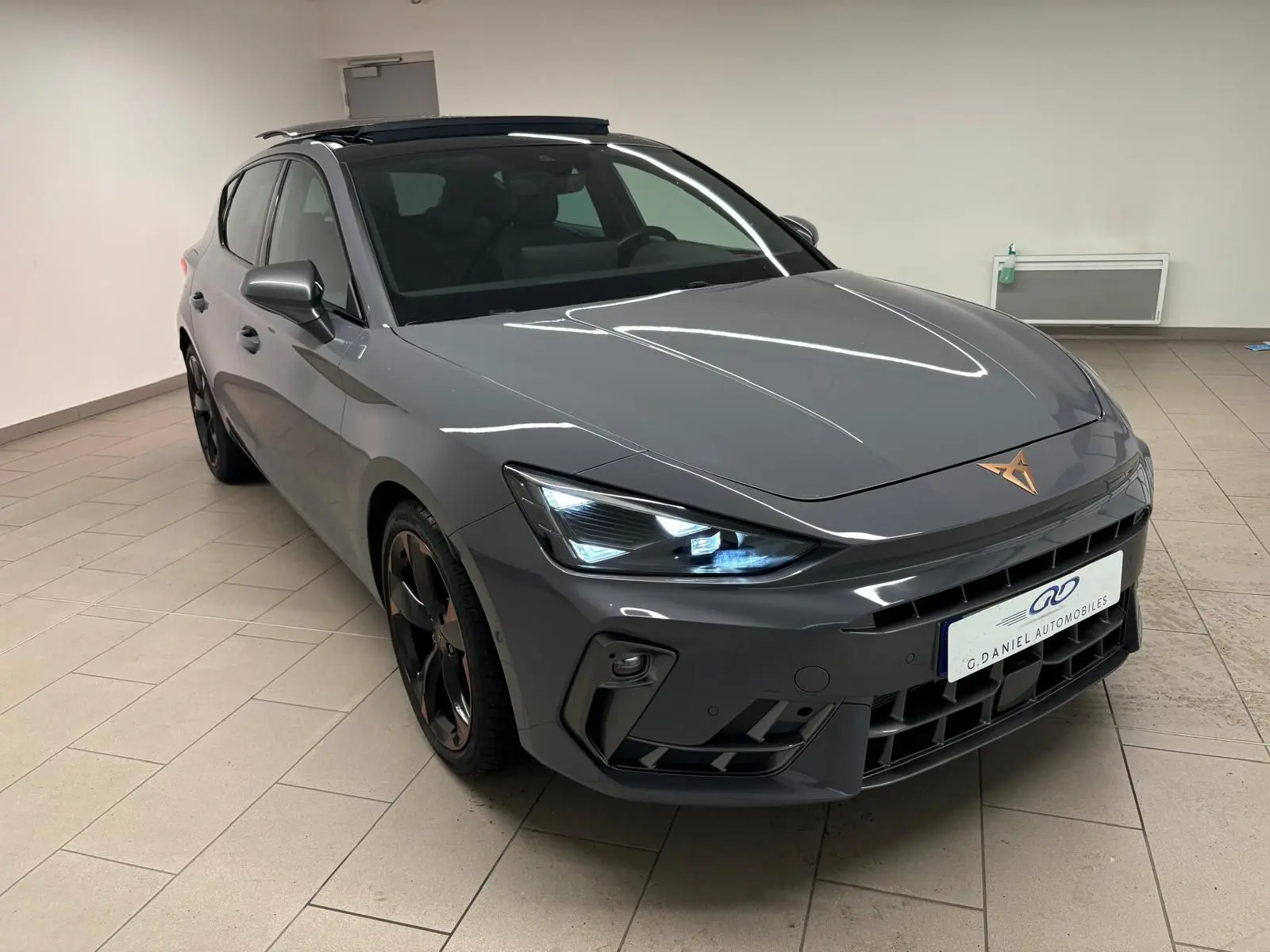 Vue 3/4 avant droit d'une CUPRA Leon gris Graphène avec toit ouvrant panoramique et jantes cuivrées en alliage 18 pouces.