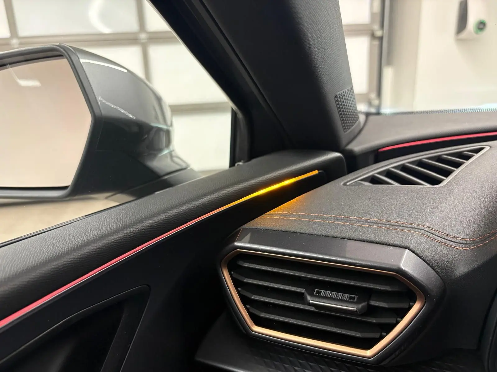 Détail intérieur côté gauche du tableau de bord de la CUPRA Leon 2025 avec éclairage d'ambiance orange et surpiqûres cuivrées.