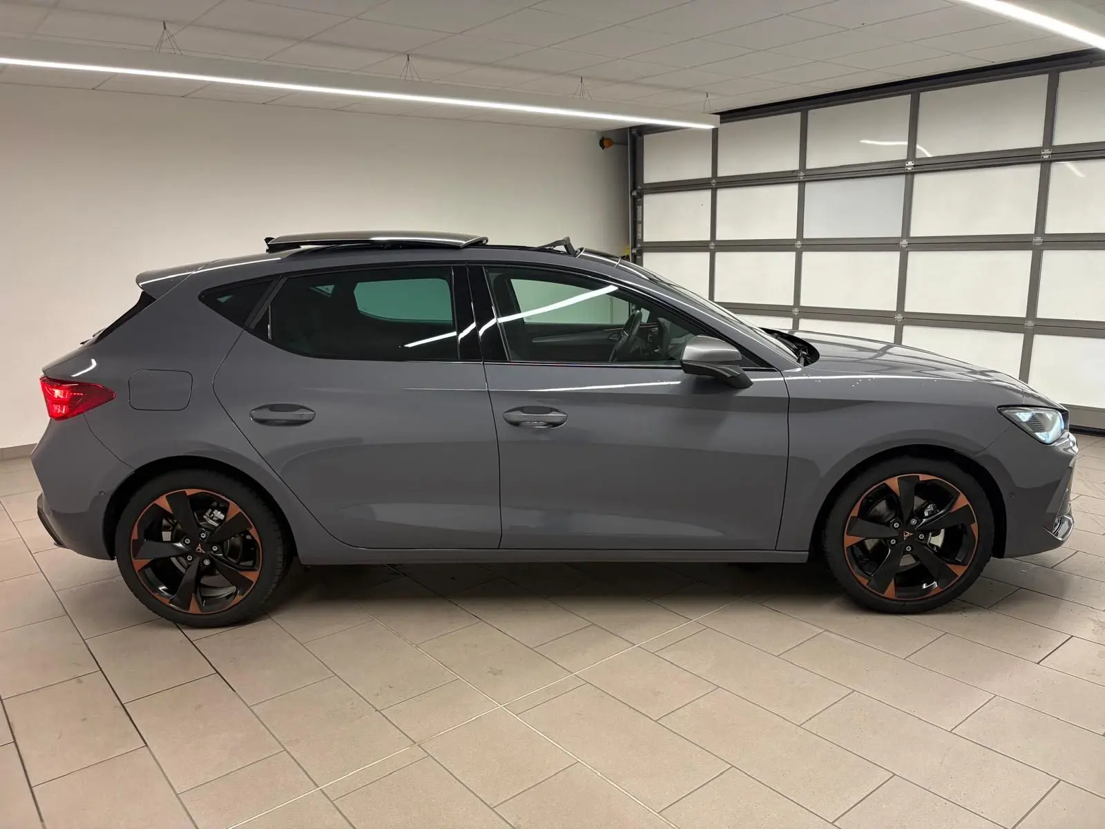 Vue de profil côté gauche d'une CUPRA Leon gris Graphène avec toit ouvrant panoramique et jantes cuivrées.