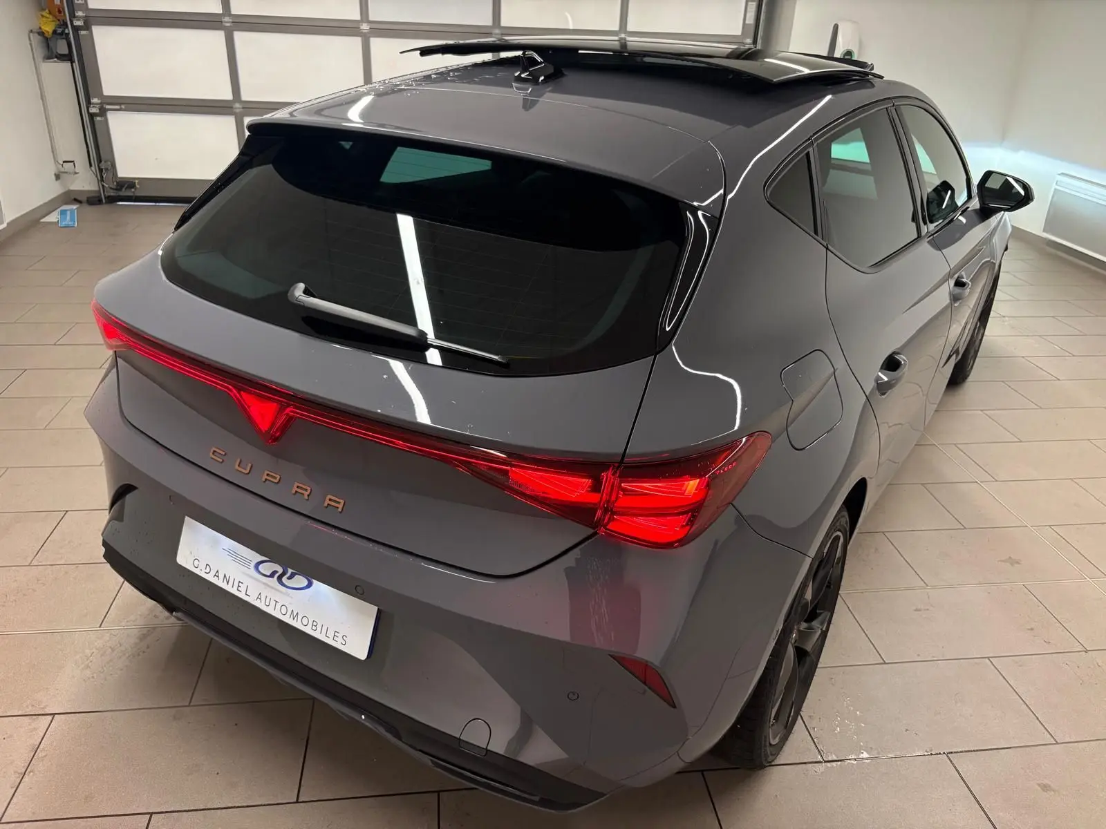 Vue 3/4 arrière droite d'une CUPRA Leon gris Graphène avec toit ouvrant panoramique et feux arrière LED allumés.