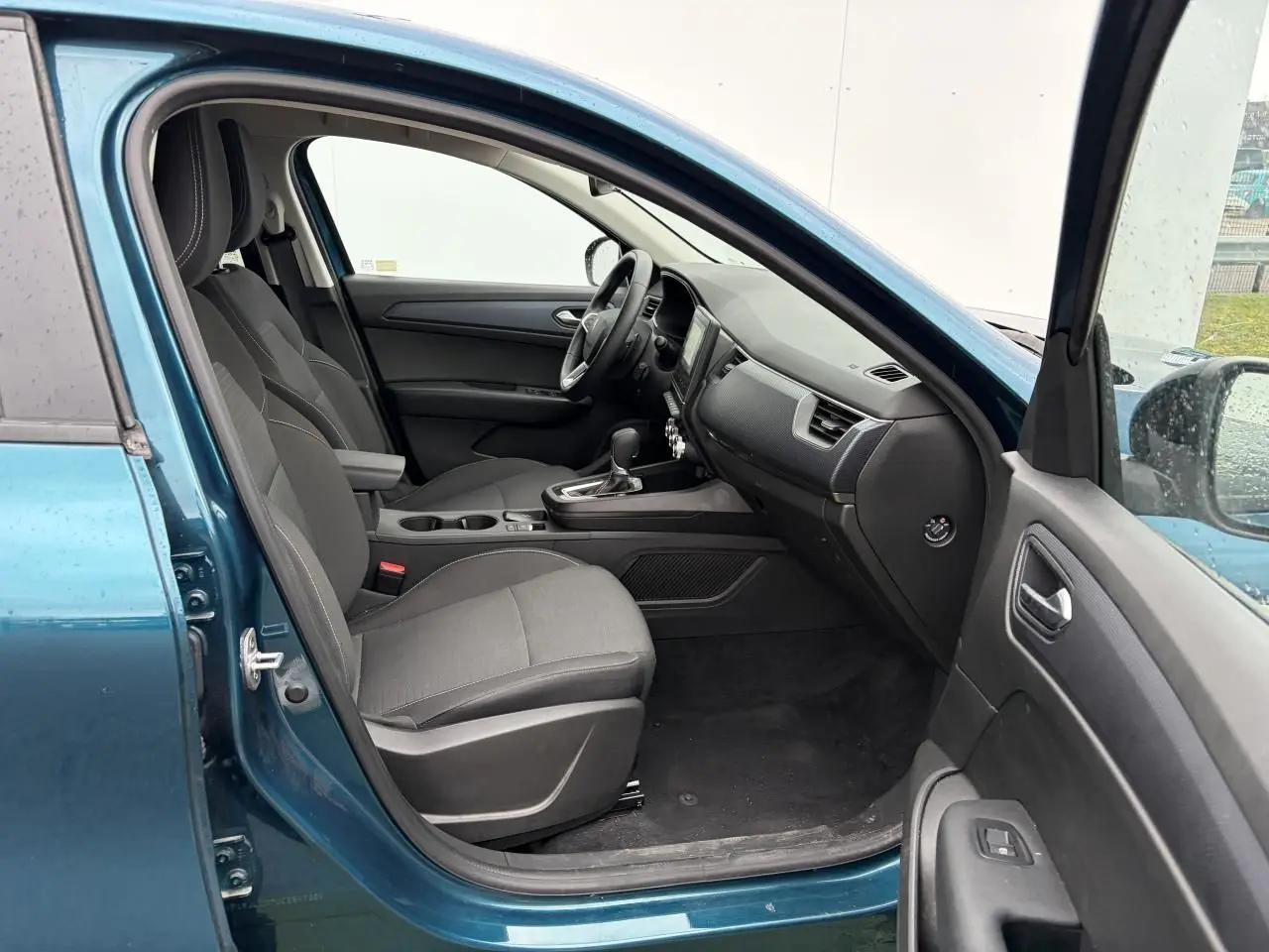 Vue intérieure côté conducteur d'une Renault Arkana 2025 bleu Zanzibar, sièges tissu gris et console centrale avec boîte auto.