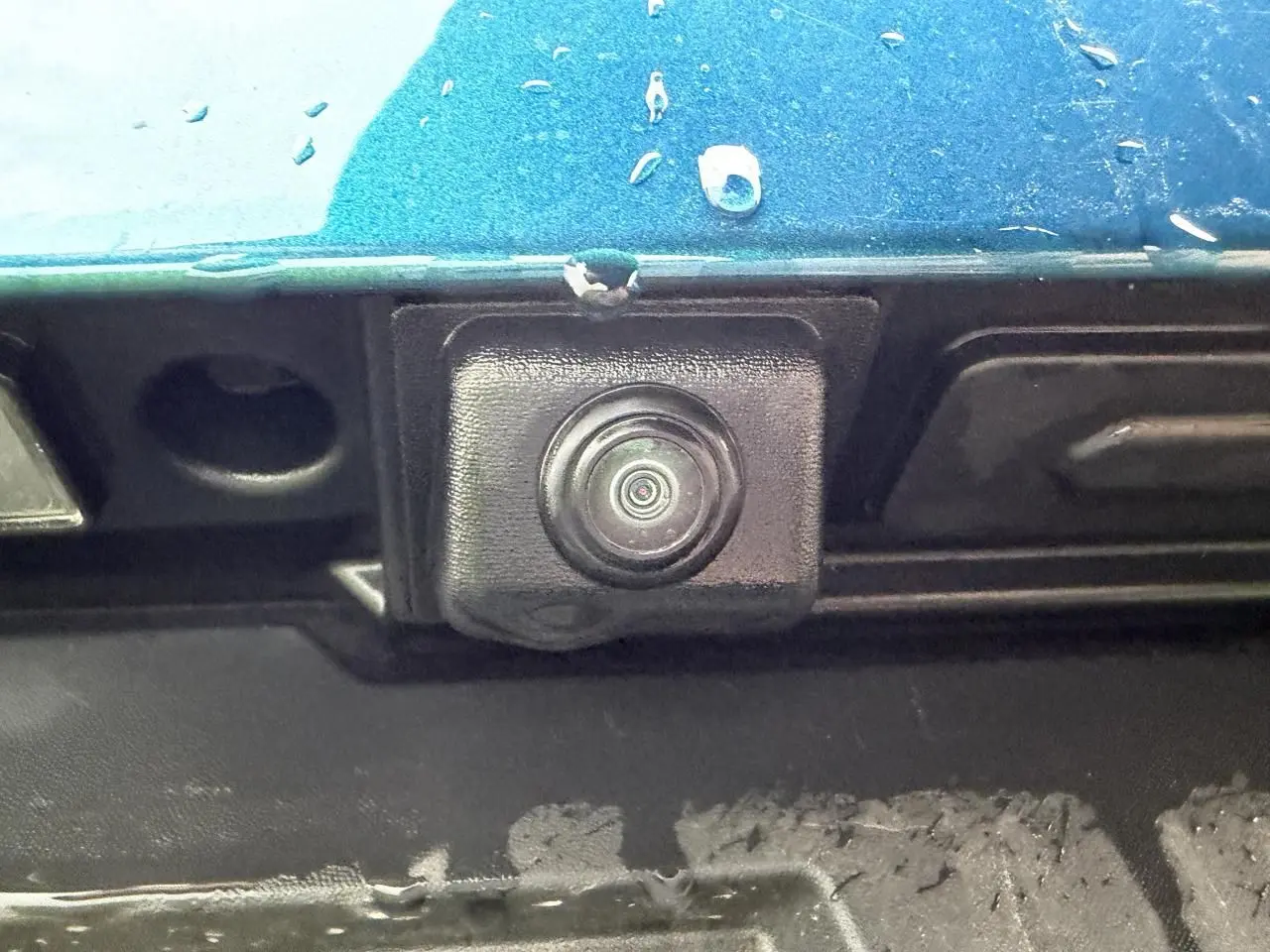 Gros plan sur la caméra de recul noire sous la peinture Bleu Zanzibar métallisée du hayon arrière du Renault Arkana 2025.