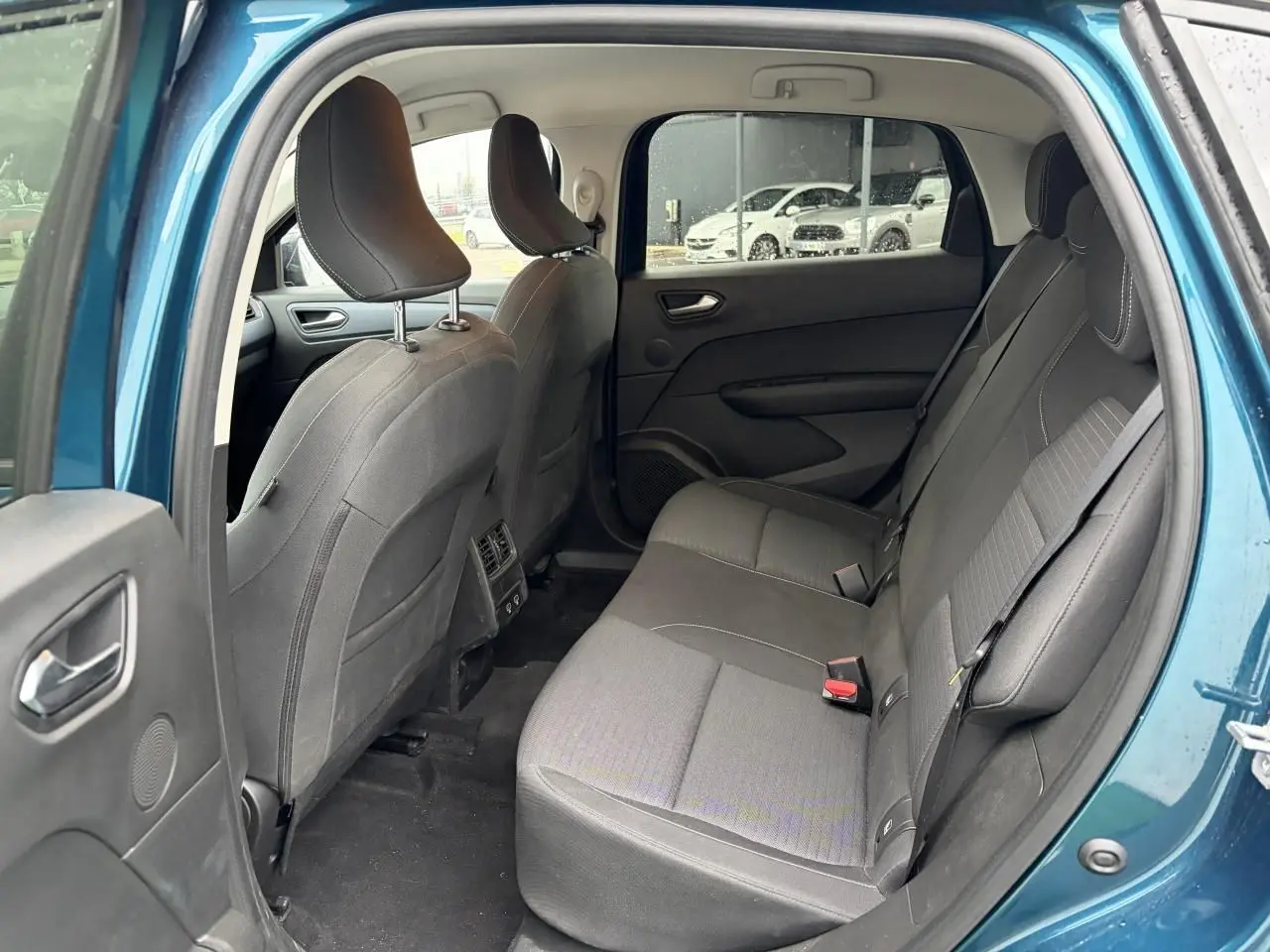 Vue intérieure arrière côté gauche du Renault Arkana bleu Zanzibar, montrant les sièges arrière en tissu gris et les portières ouvertes.