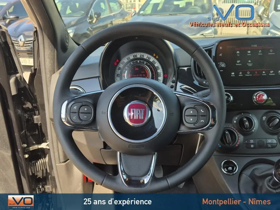 Vue intérieure centrée sur le volant noir de la FIAT 500C 2024 avec tableau de bord et commandes visibles.