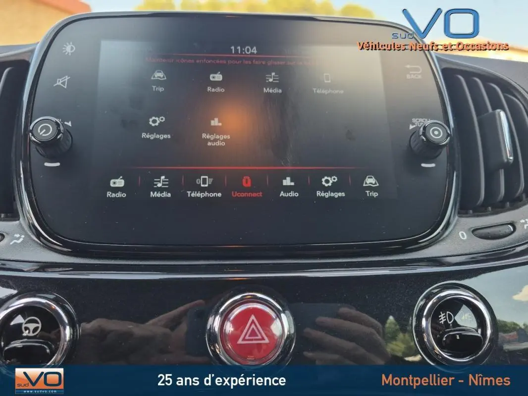 Écran tactile central et commandes de la console d’une Fiat 500C noire, version hybride 2024, vue intérieure frontale.