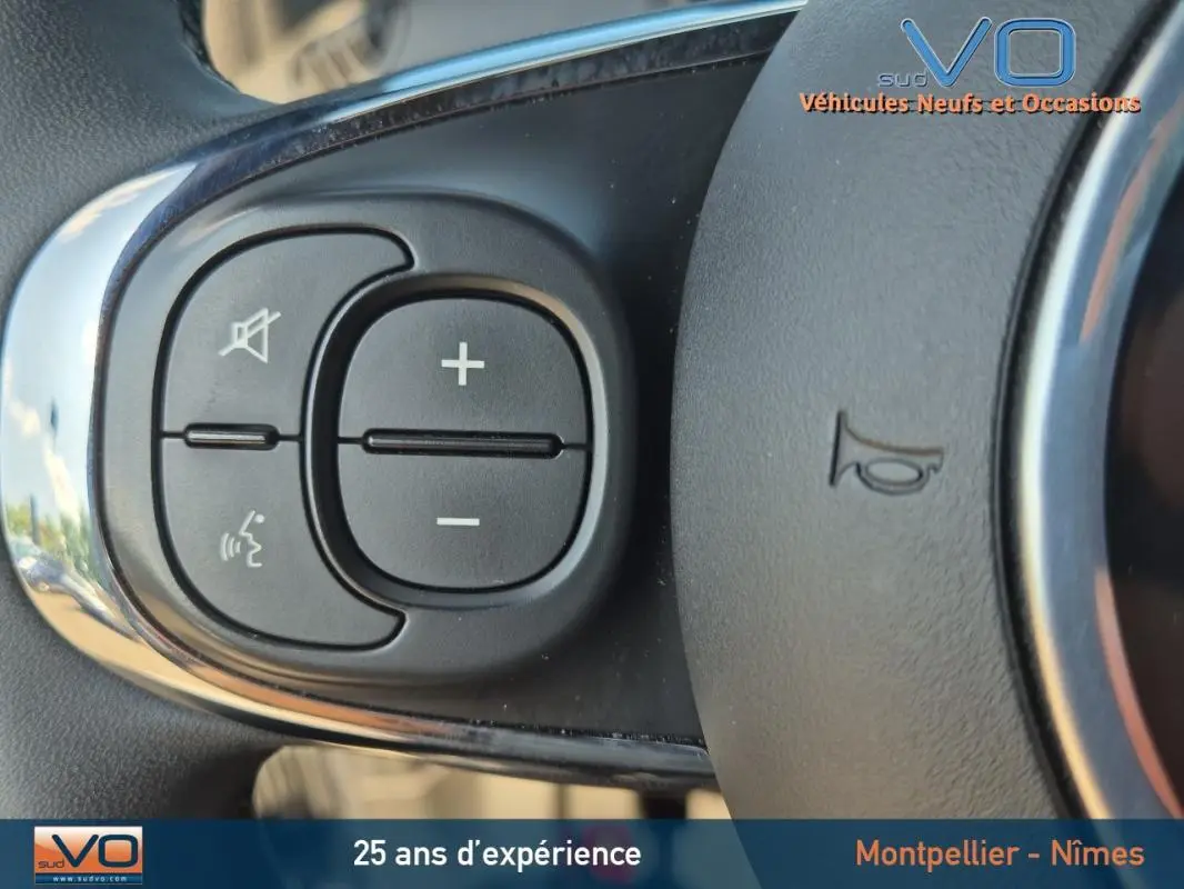 Gros plan sur les commandes de volume et de téléphone au volant noir de la FIAT 500C 2024 hybride.