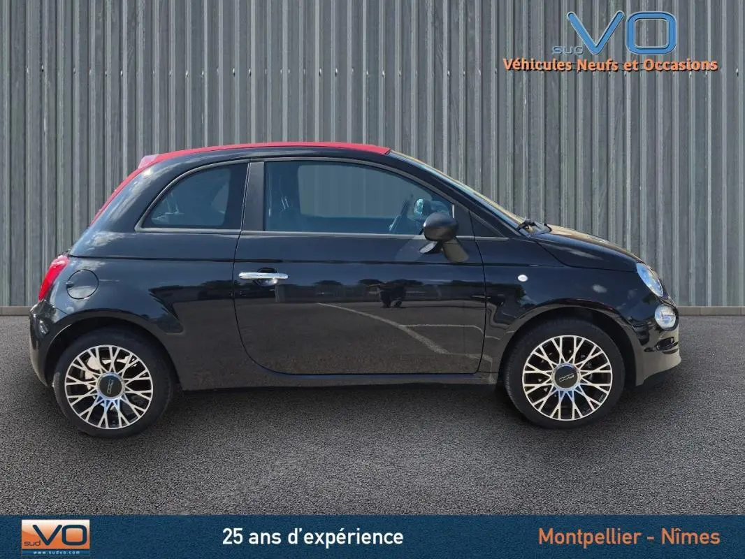 Profil côté gauche de la FIAT 500C noire 2024 avec toit rouge et jantes alliage 15 pouces, sur fond industriel.