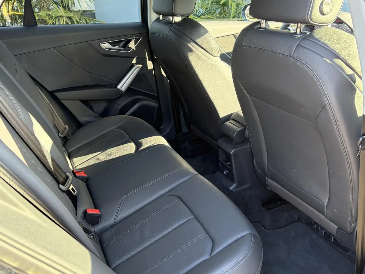 Vue intérieure arrière côté gauche de l'Audi Q2 35 TFSI S-Line 2024 avec sièges en cuir noir et finitions modernes.