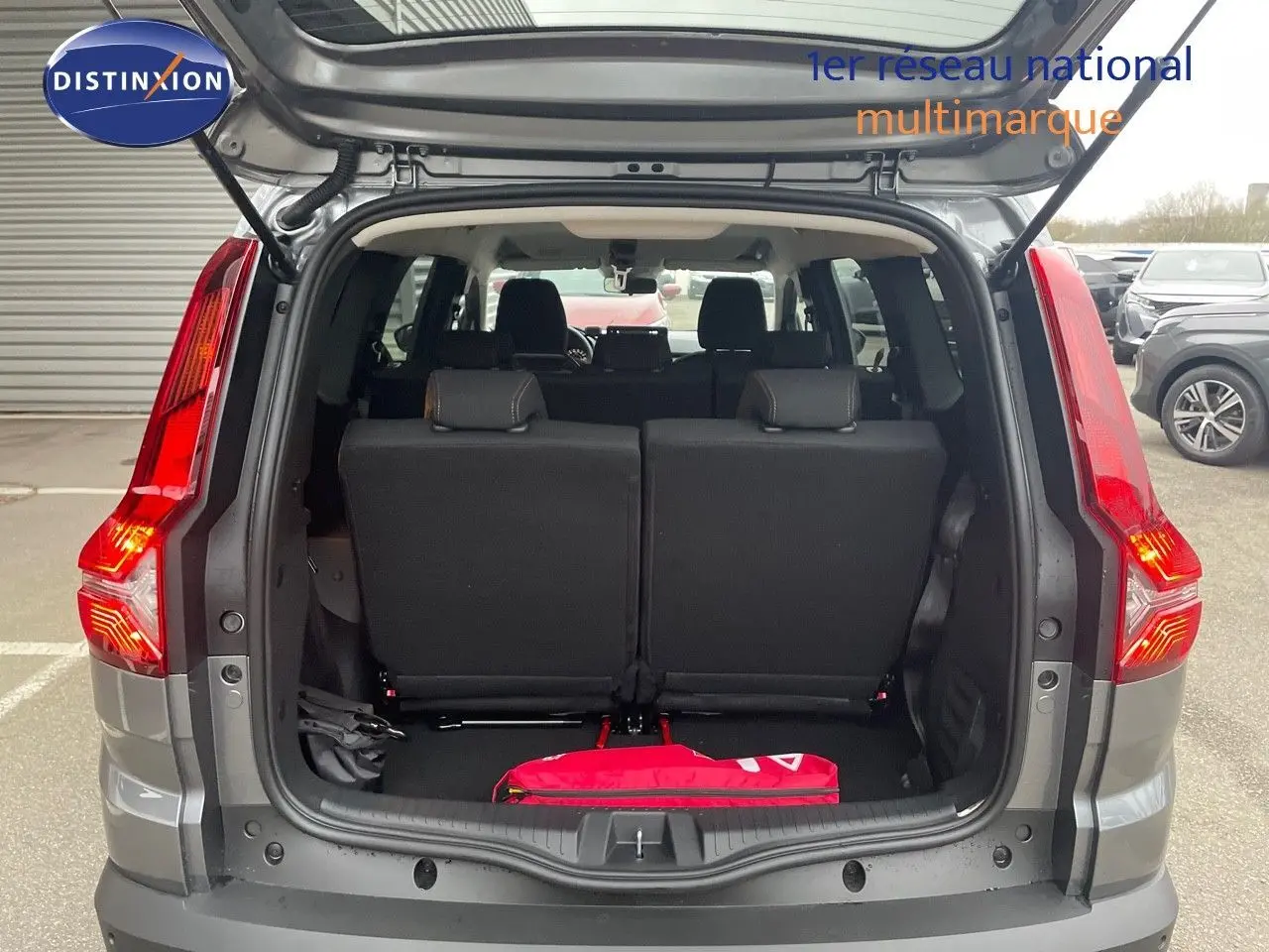 Vue arrière ouverte du Dacia Jogger gris schiste métal 2026, montrant les sièges arrière et un objet rouge dans le coffre.