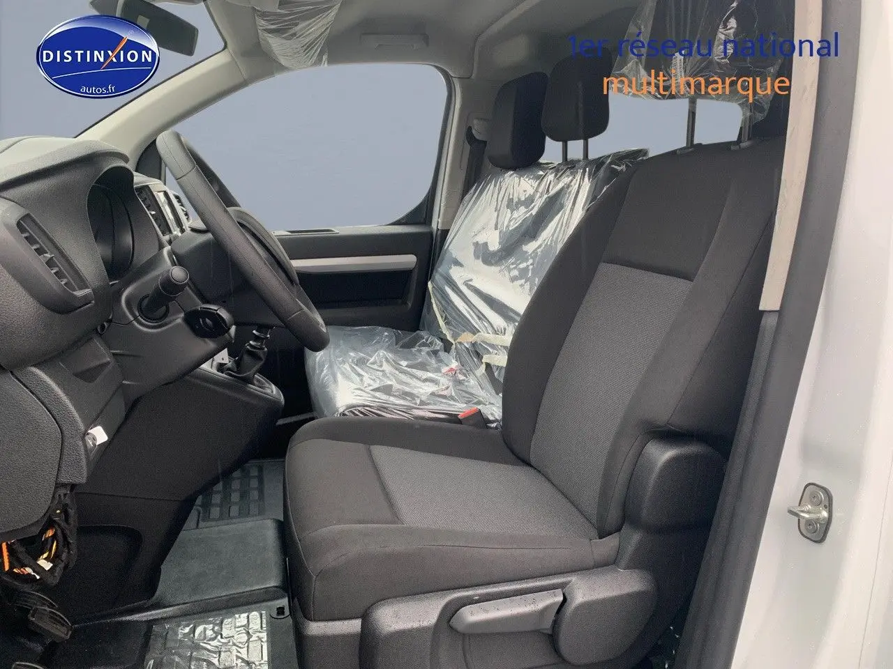 Vue intérieure côté conducteur du Peugeot Expert Long blanc 2023, sièges noirs avec protections plastiques visibles.