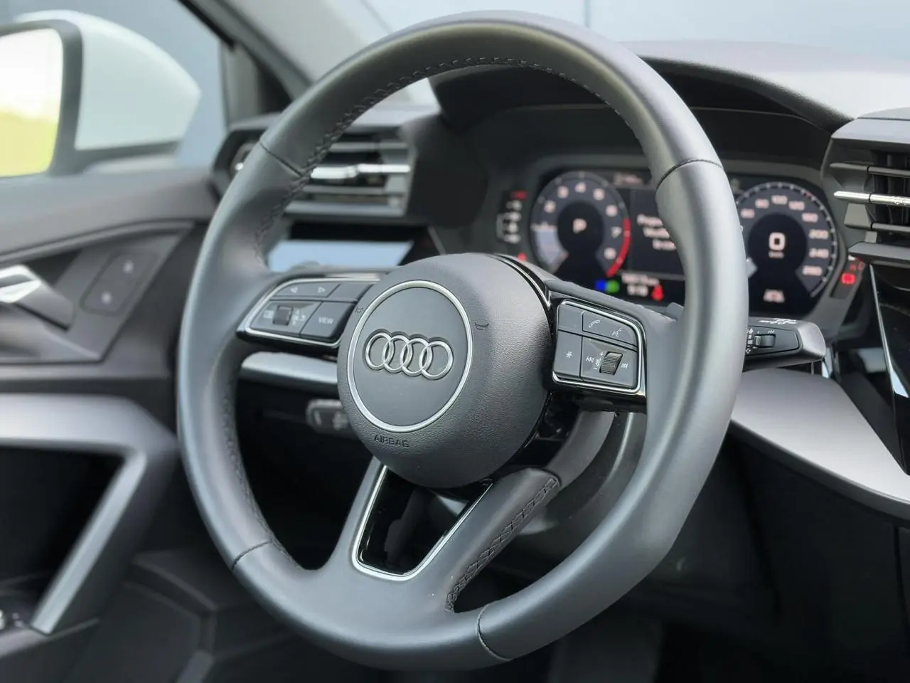 Volant cuir 3 branches multifonctions de l'Audi A3 Sportback 2024 vu de face côté conducteur, avec tableau de bord numérique.