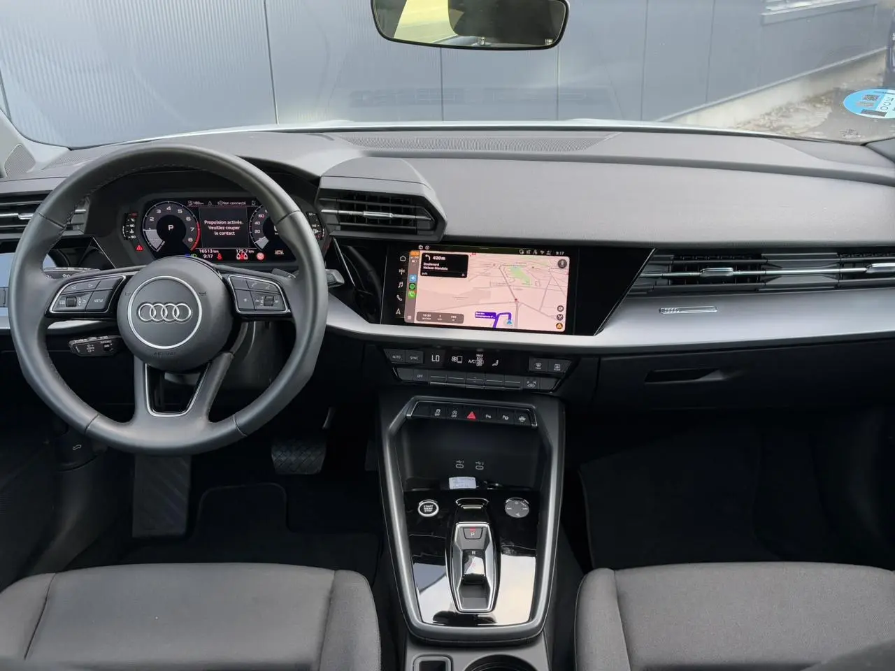 Vue intérieure du tableau de bord et volant cuir de l'Audi A3 Sportback 2024 avec écran tactile et console centrale noire brillante.