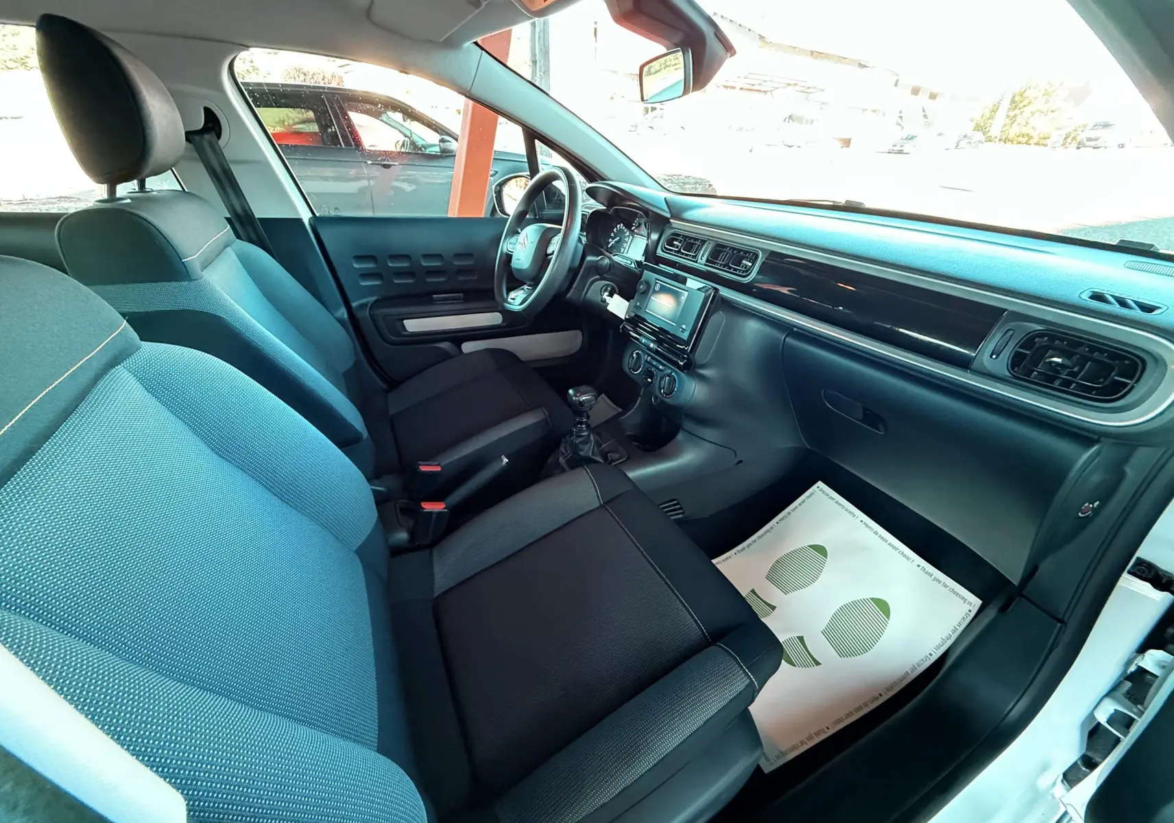 Intérieur côté conducteur d'une Citroën C3 blanche 2021, sièges tissu gris noir et tableau de bord moderne noir.