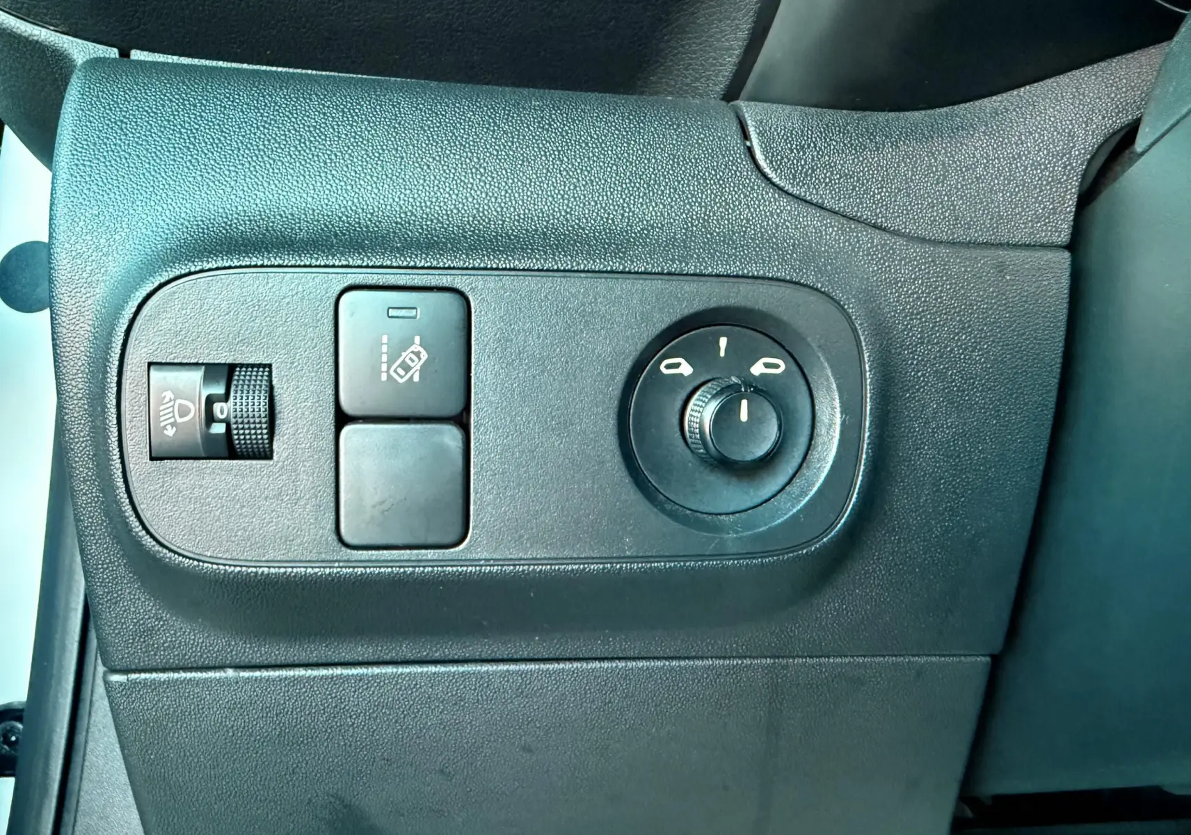 Vue rapprochée des commandes de réglage des rétroviseurs et phares sur le côté gauche intérieur d'une Citroën C3 blanche.