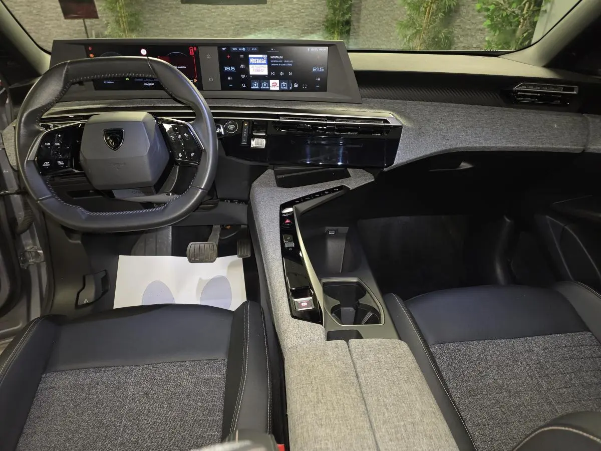 Vue intérieure avant du Peugeot 3008 Hybrid 2025, tableau de bord et console centrale avec décor tissu gris et noir laqué.