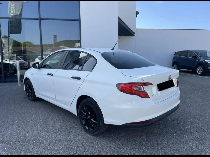Fiat Tipo blanc en 3/4 arrière droit avec jantes noires, garée devant un bâtiment vitré.