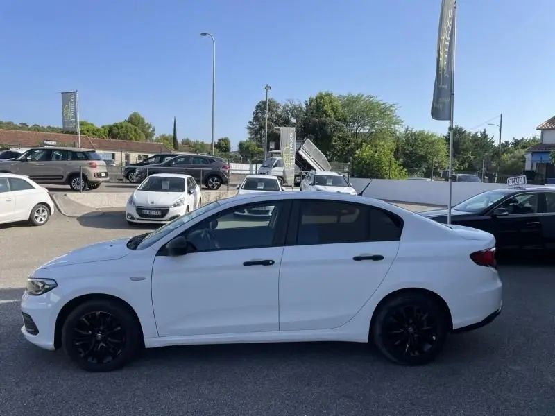 Vue latérale côté gauche d'une Fiat Tipo blanche 2019 avec jantes noires, garée en extérieur sur un parking.