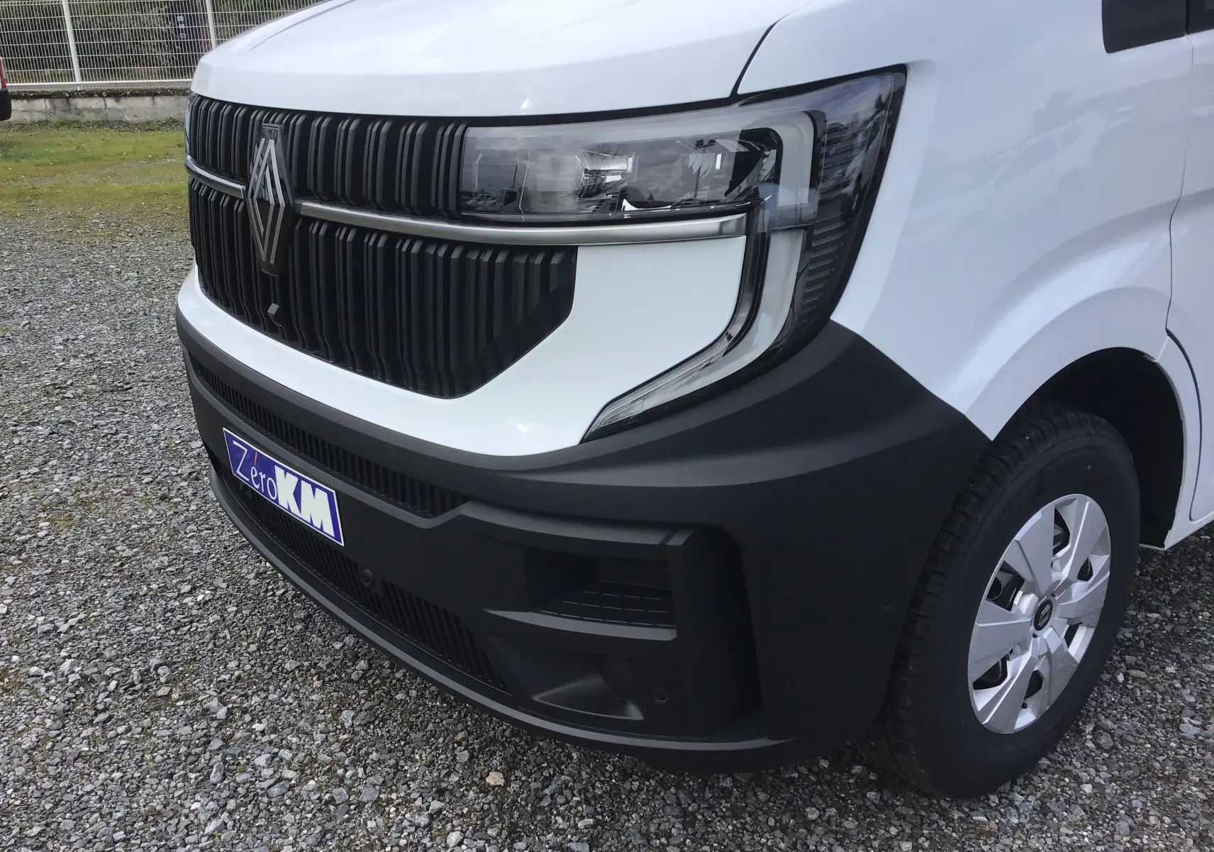 Vue avant droite du Renault Master blanc 2025 avec calandre noire et pare-chocs noir mat, sur sol gravillonné.