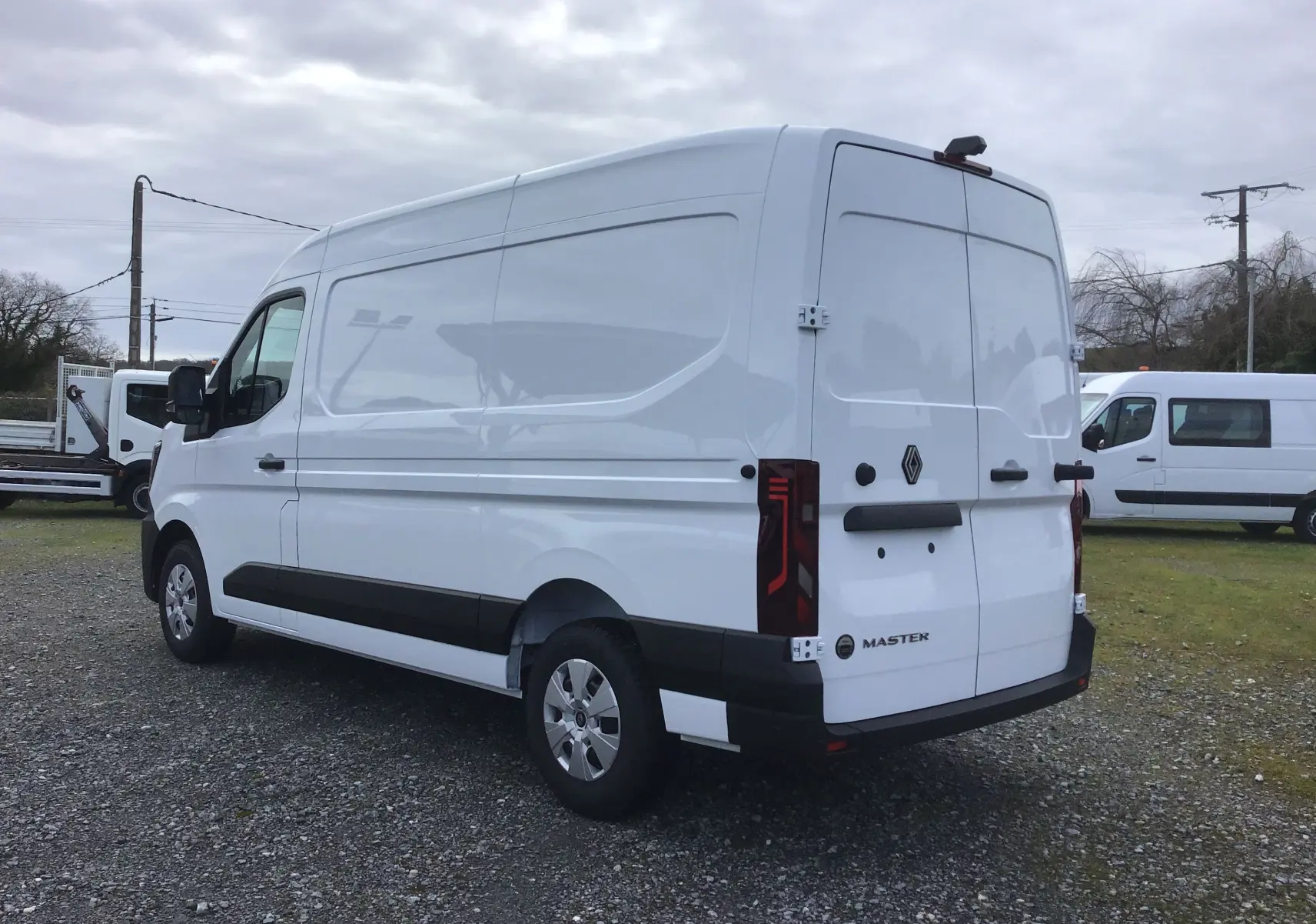Renault Master blanc en vue 3/4 arrière droit, avec hayon fermé et bandeau noir sur les flancs.