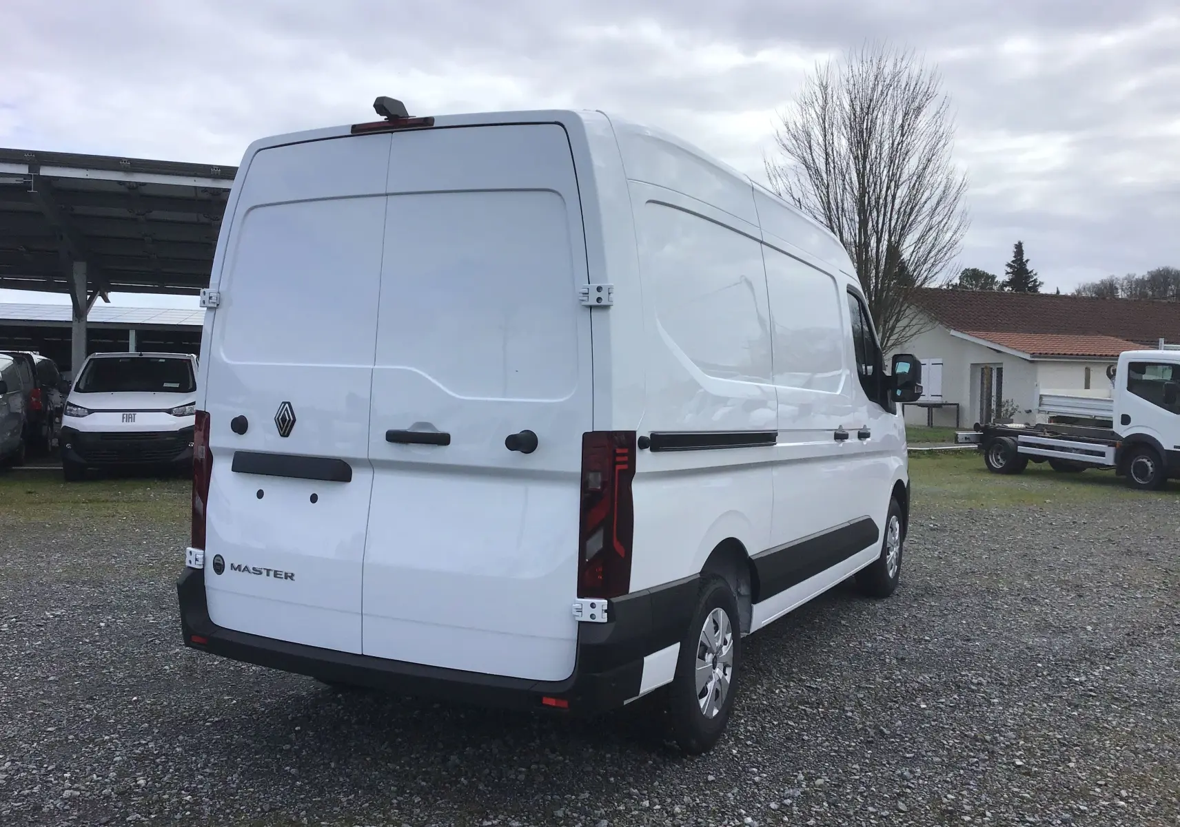 Renault Master blanc vu en 3/4 arrière droit, fourgon utilitaire avec feux arrière verticaux et protections noires.