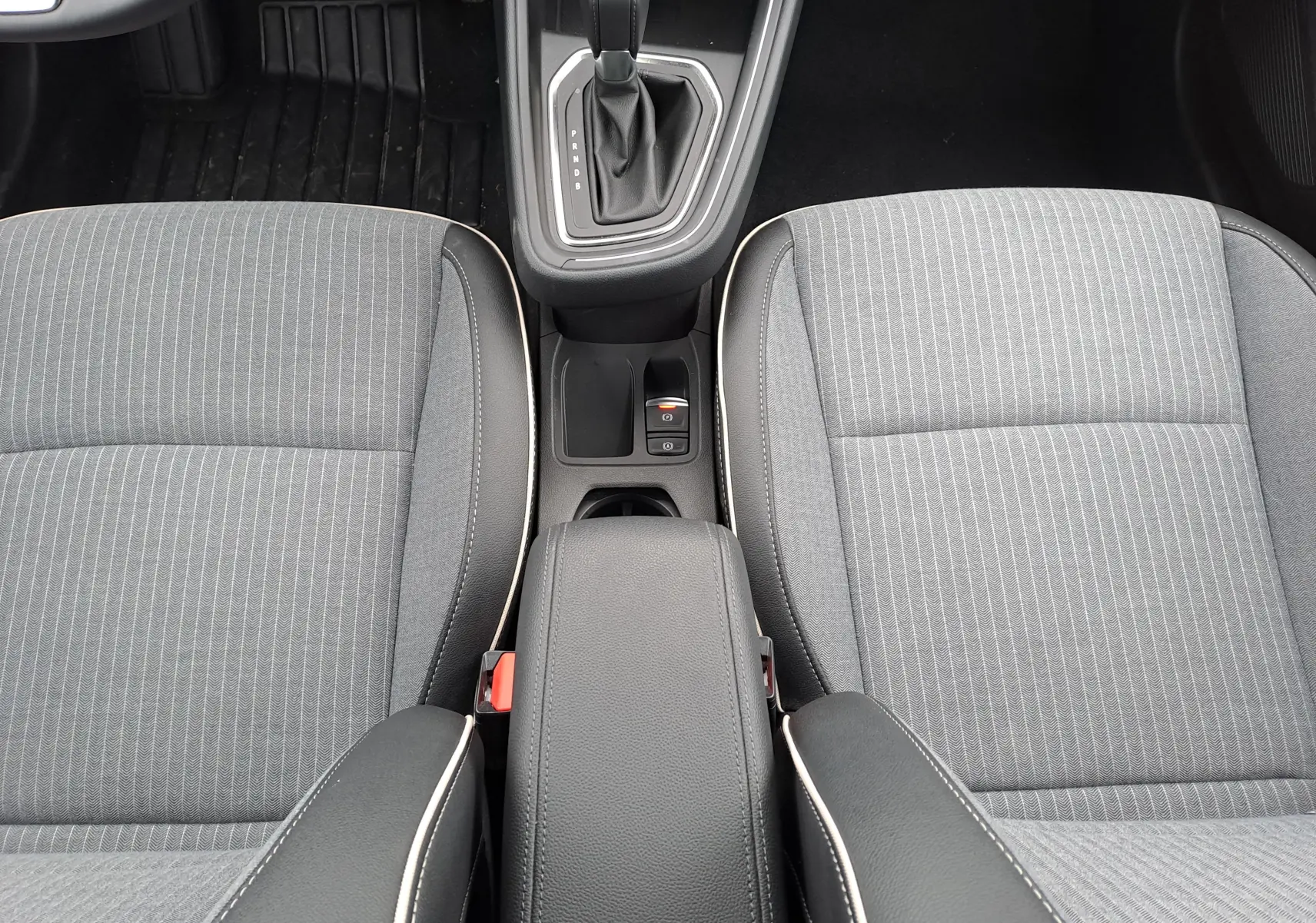 Vue intérieure centrée sur la console centrale et les sièges avant gris à surpiqûres blanches de la Renault Clio V hybride.