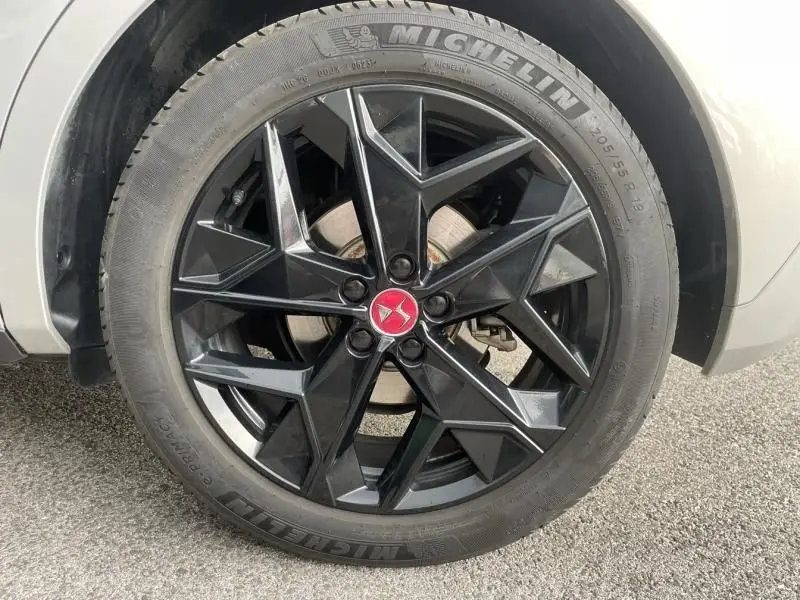 Gros plan sur la roue avant gauche du DS4 gris 2023, jante noire au design géométrique avec logo DS rouge au centre.