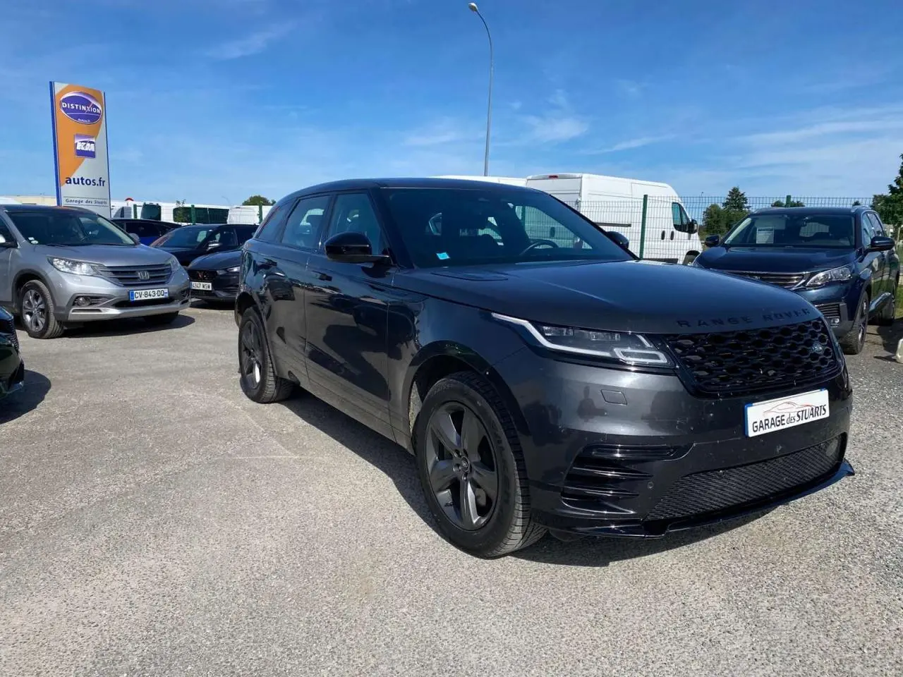 Range Rover Velar gris tempête vu en 3/4 avant droit avec jantes satinées et calandre noire brillante.
