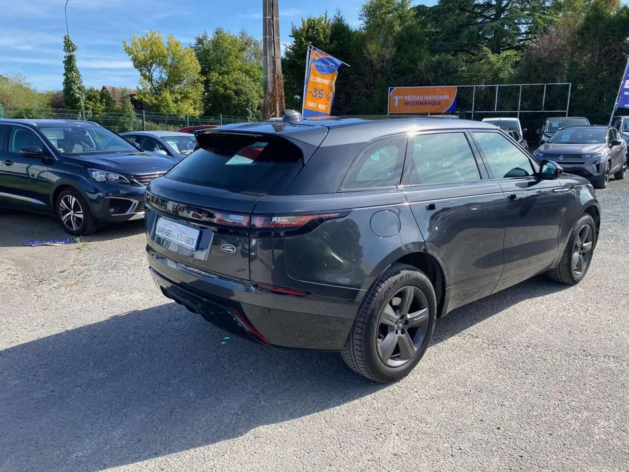 Vue 3/4 arrière droite du Range Rover Velar gris Tempête avec jantes satinées et toit panoramique visible en extérieur.