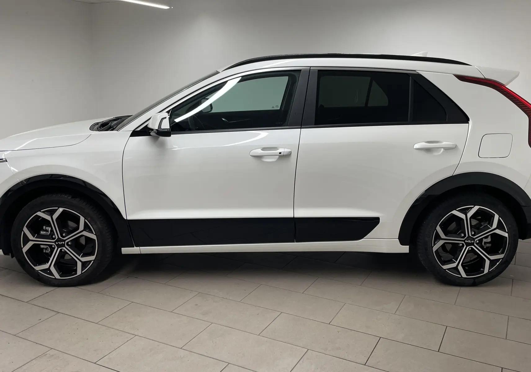 Vue de profil côté gauche du KIA NIRO 2025 blanc hybride avec jantes alliage noires et détails noirs contrastants.