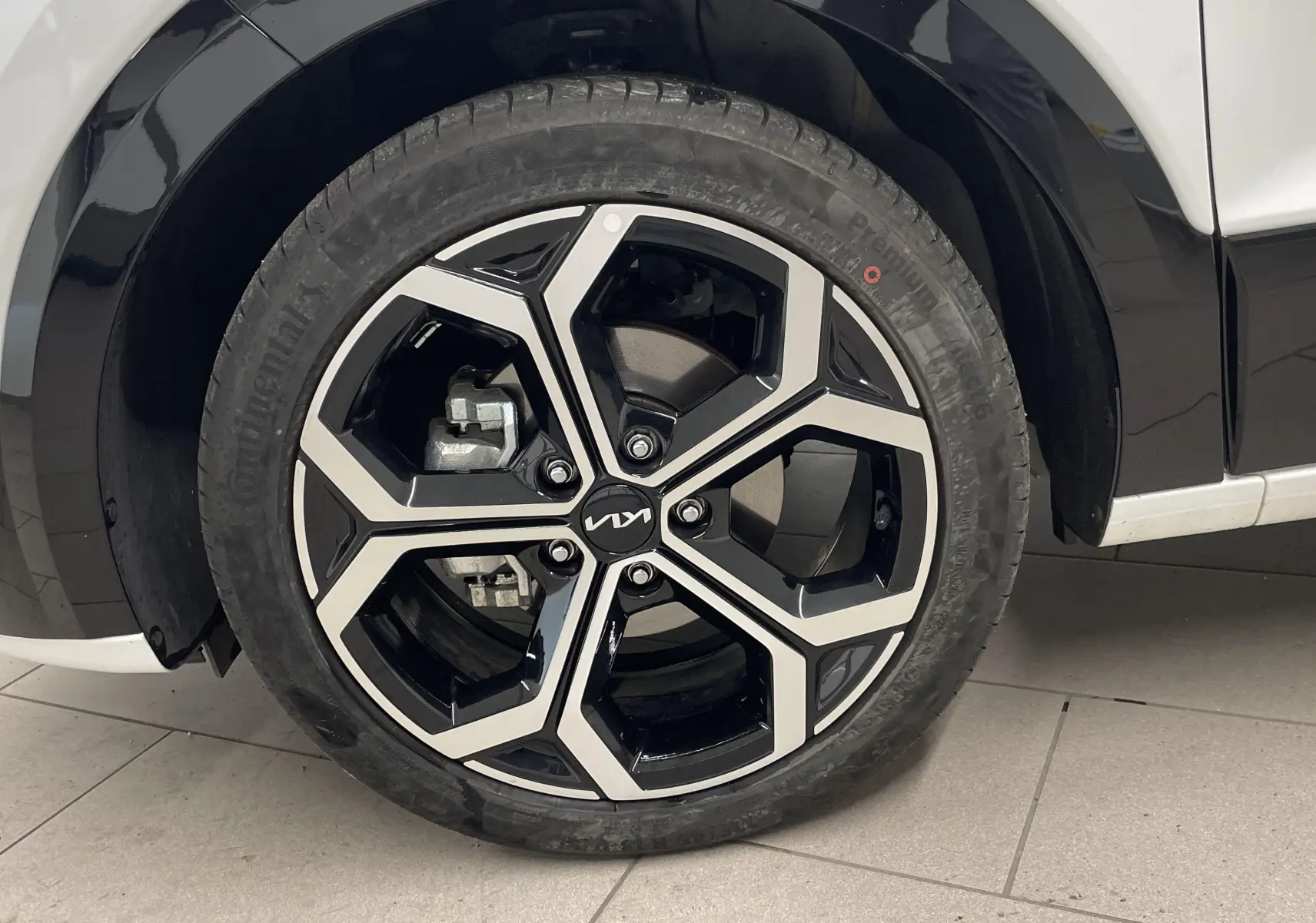 Gros plan sur la roue avant gauche d’un KIA NIRO blanc 2025, mettant en valeur la jante noire et argentée au design moderne.