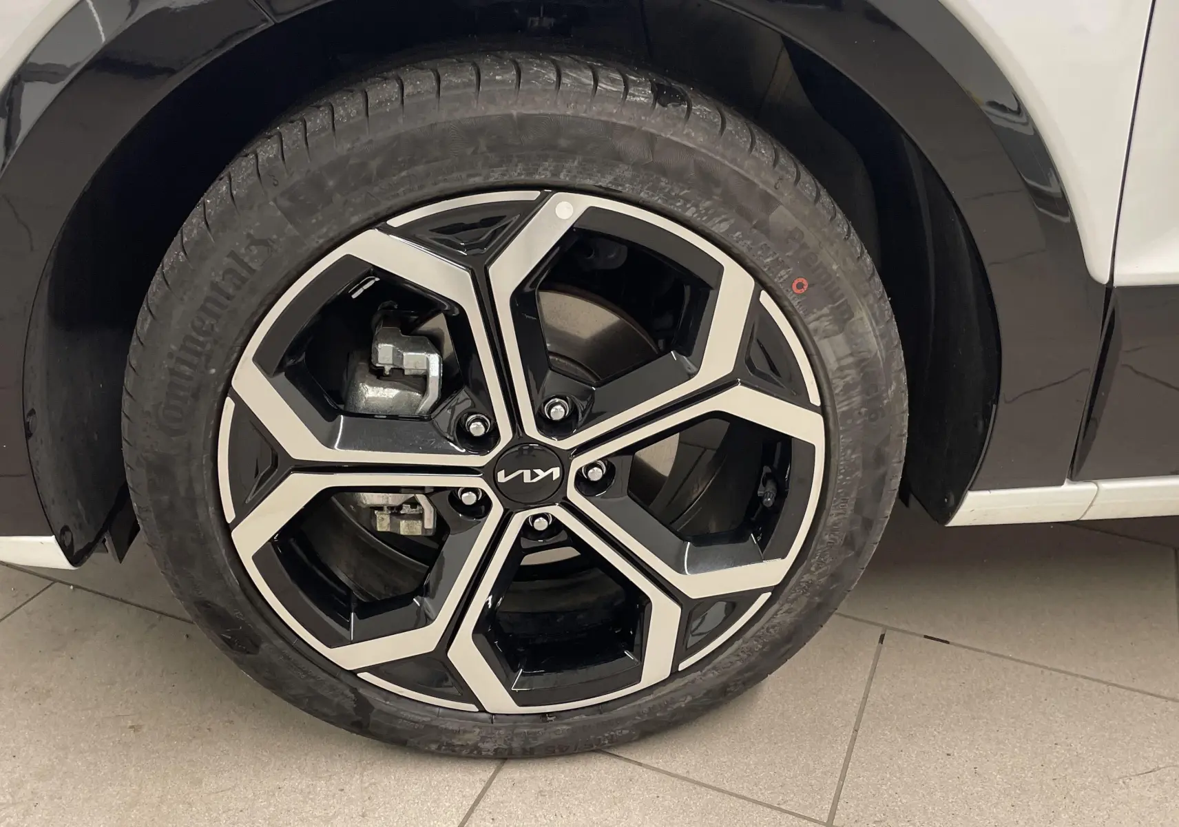 Gros plan sur la roue avant gauche du KIA NIRO blanc 2025, mettant en valeur la jante alliage noire et argentée au design moderne.