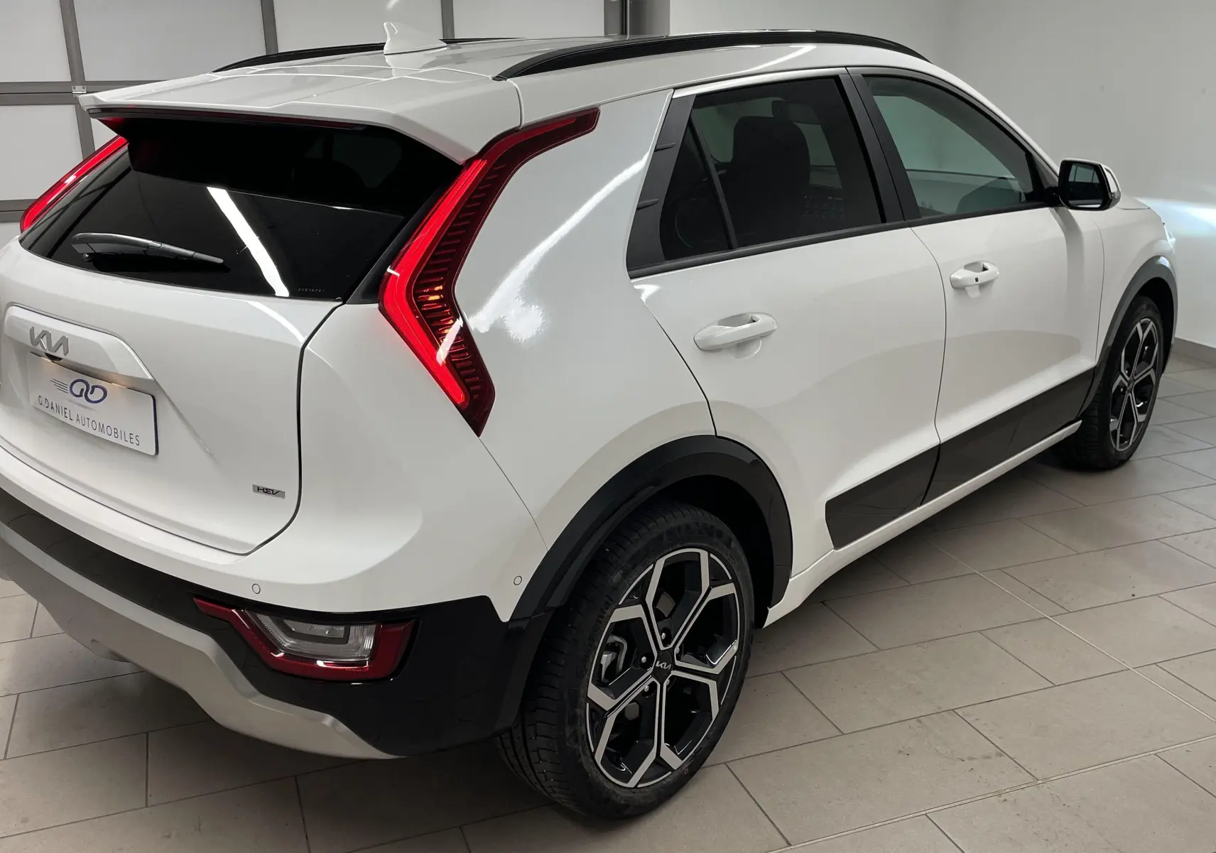 Vue 3/4 arrière droite du Kia Niro blanc 2025 hybride avec feux arrière en forme de boomerang et jantes noires.