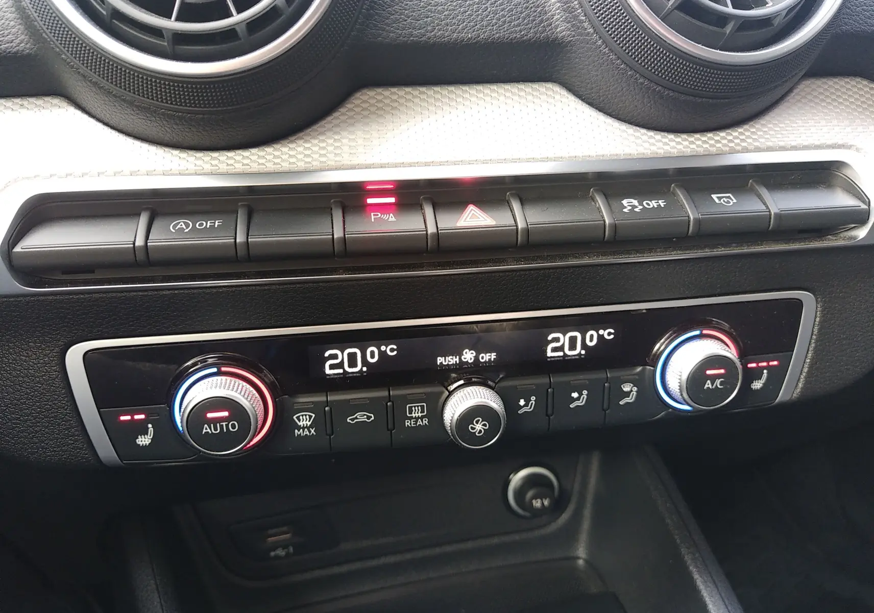 Vue rapprochée de la console centrale noire de l'Audi Q2 35 TFSI 2023, montrant les commandes de climatisation digitale et boutons fonctionnels.