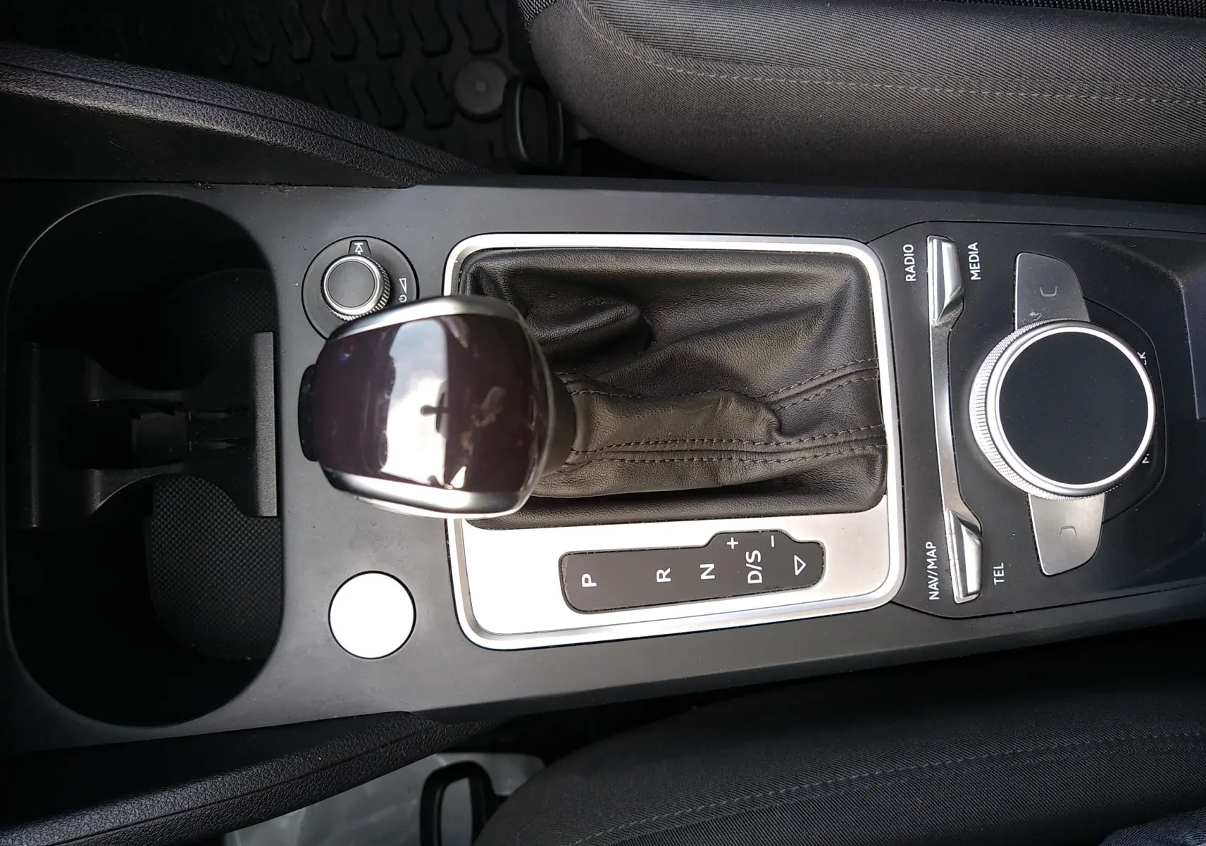 Vue rapprochée de la console centrale de l'Audi Q2 noire, mettant en valeur le levier de vitesses automatique et la molette de contrôle multimédia.