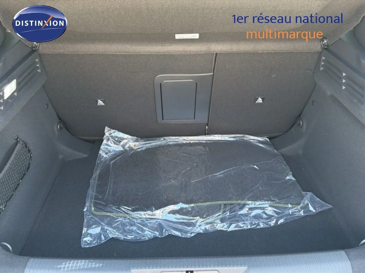 Coffre ouvert d’une Peugeot 308 Hybrid 145ch GT noir perle métal, avec tapis de sol emballé visible au centre.