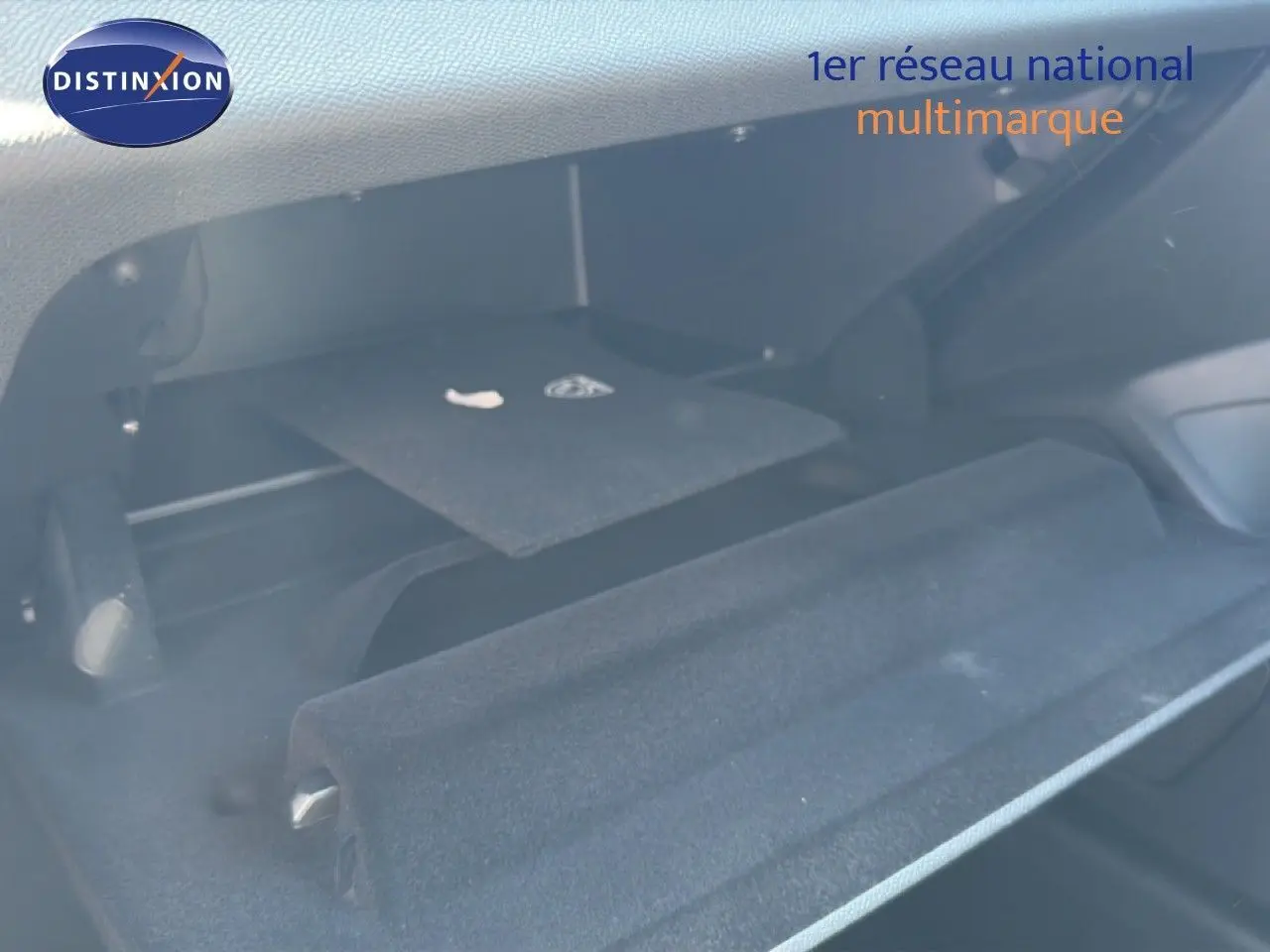 Intérieur du coffre ouvert d'une Peugeot 308 Hybrid 145ch GT noir perle métal, montrant le tapis de sol et compartiments.
