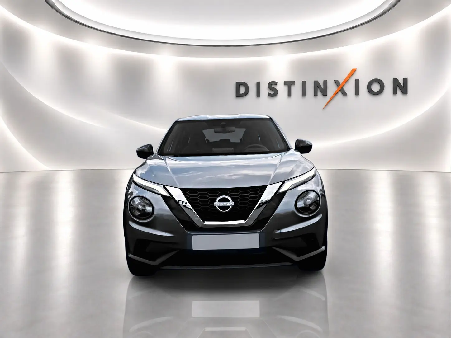 Vue avant d'un Nissan Juke gris 2025 dans un showroom avec éclairage moderne et logo Distinxion en arrière-plan.