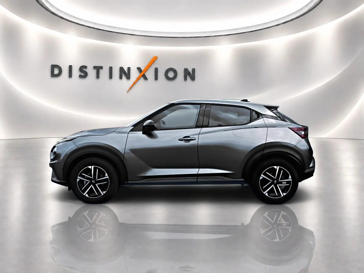 Profil droit d'un Nissan Juke 2025 gris avec jantes alliage noires, dans un showroom lumineux au mur blanc.