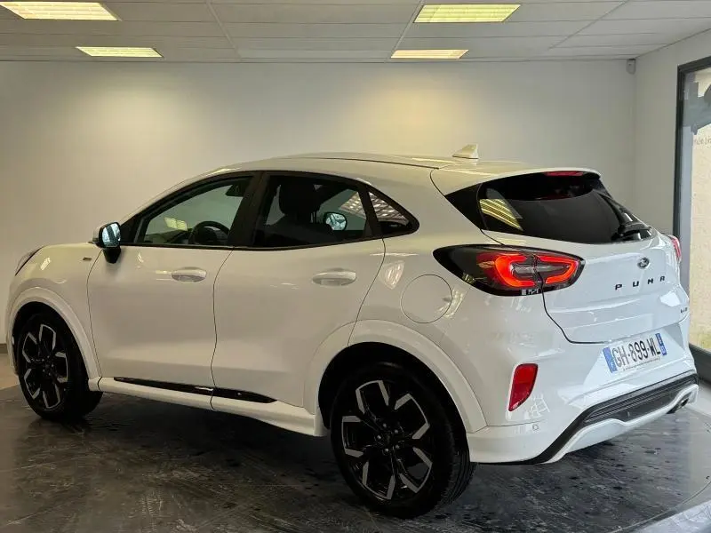 Vue 3/4 arrière droite d'un Ford Puma blanc Glacier avec jantes noires et feux arrière LED allumés dans un showroom.