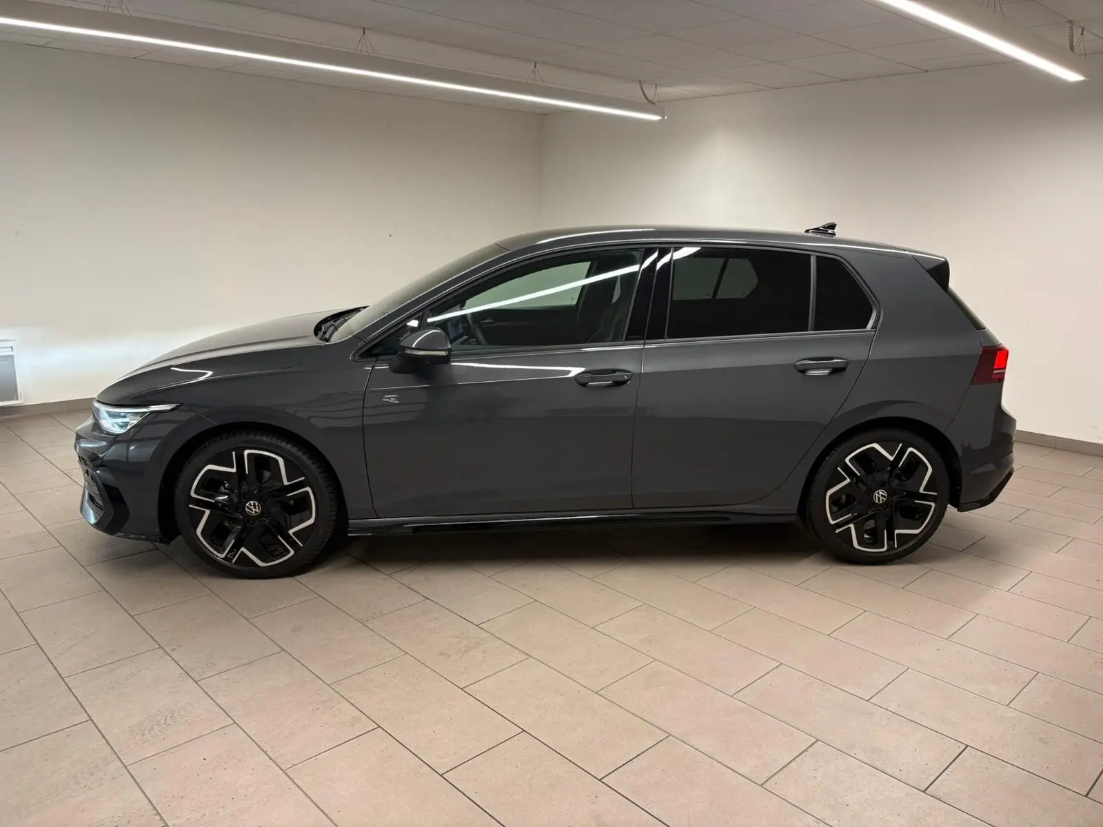 Vue de profil côté gauche d'une Volkswagen Golf 1.5 eTSI 150 DSG7 R-Line Edition gris dauphin en intérieur, avec jantes spécifiques R-Line.