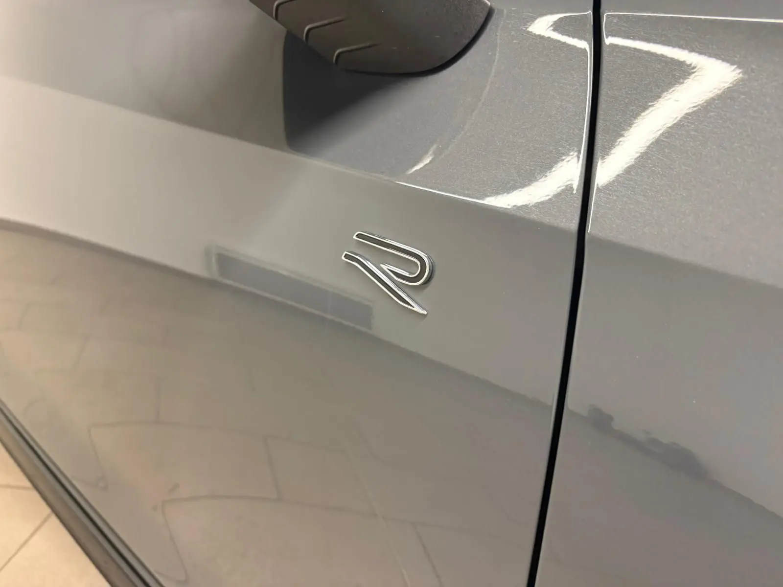 Gros plan sur l'emblème R sur la porte côté gauche d'une Volkswagen Golf gris dauphin brillante.